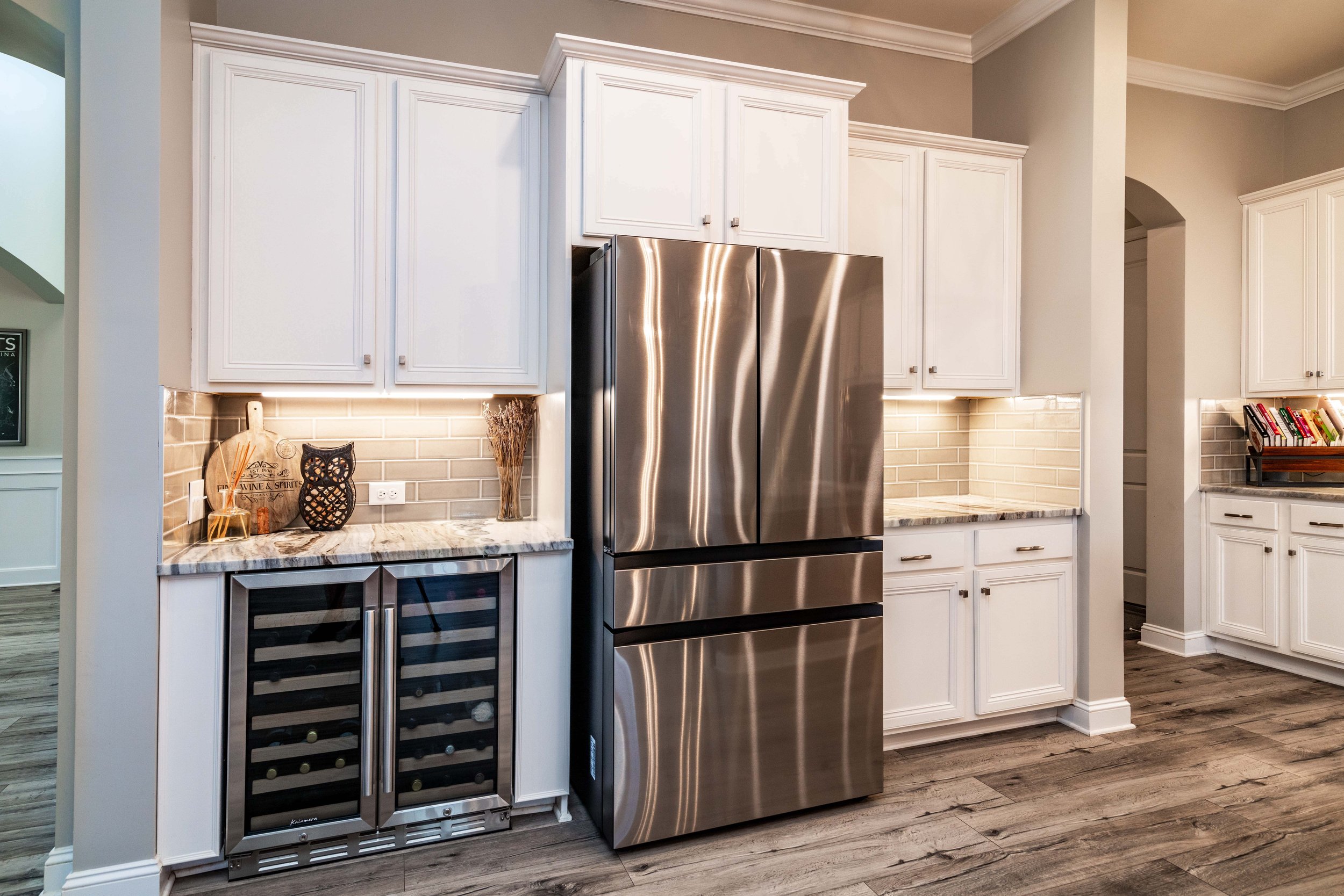Modern kitchen with a sleek stainless steel refrigerator, white cabinets, and marble countertops. Soft lighting creates a warm, inviting atmosphere.