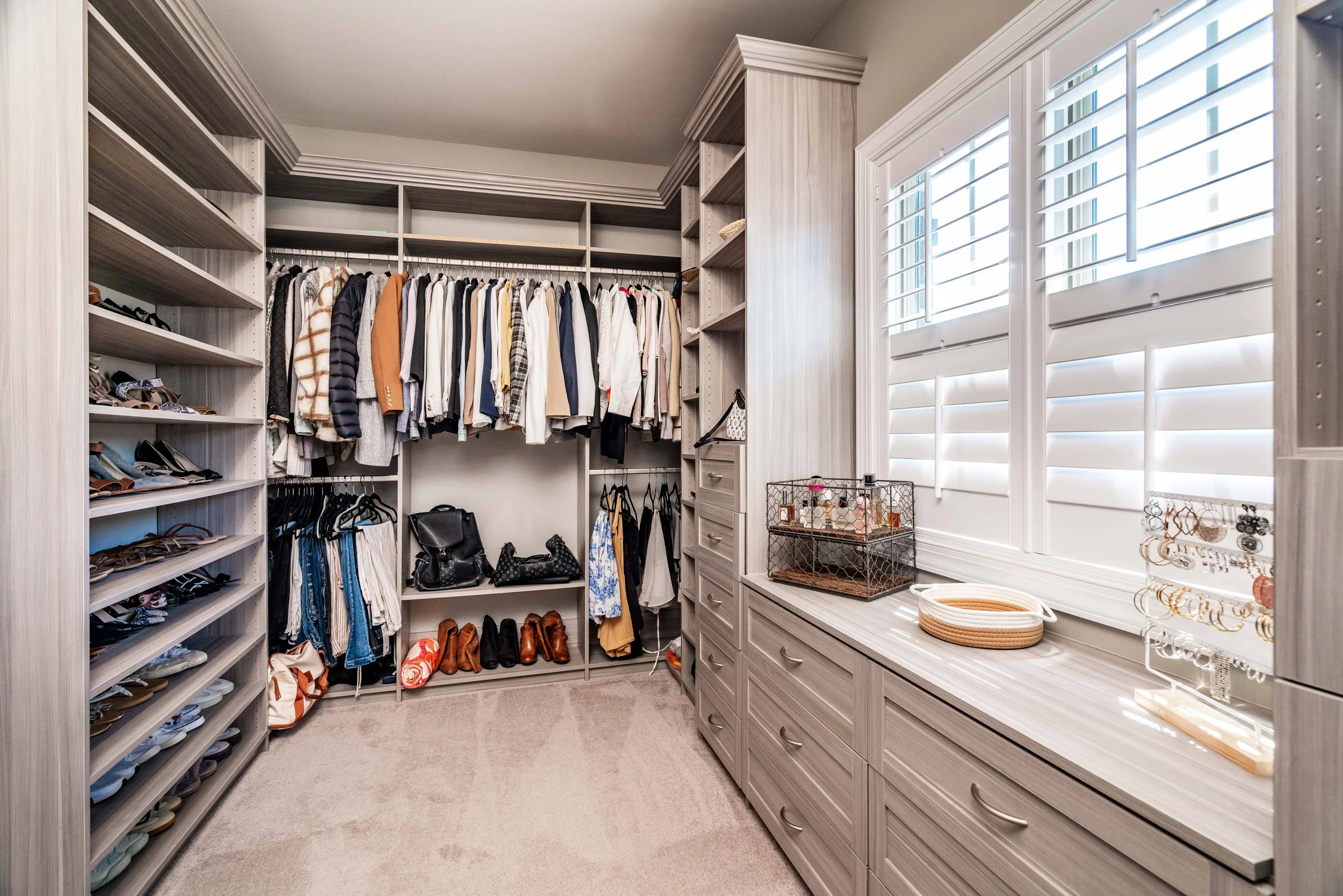 Luxurious walk-in closet with neatly organized clothes on hangers, shoes on shelves, jewelry on display, and soft lighting creating a serene atmosphere.