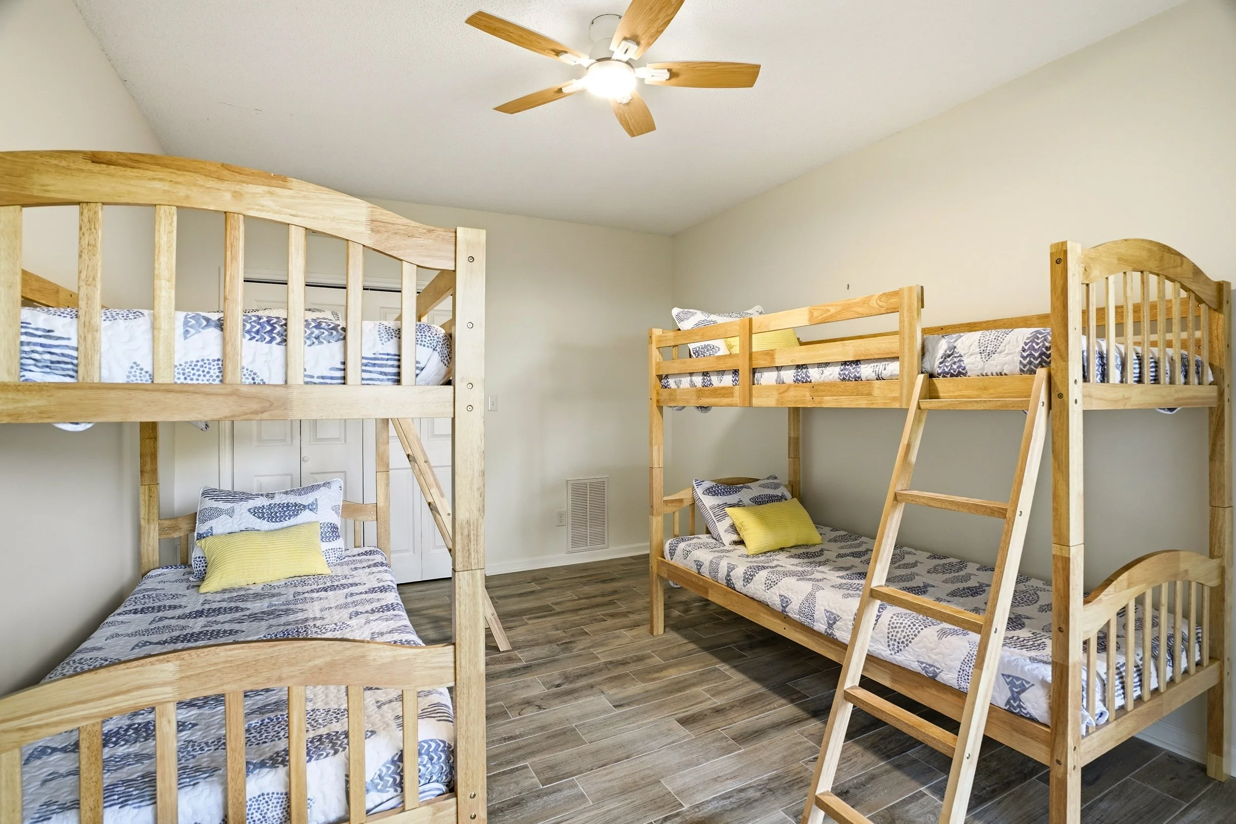 Bright bedroom with wood-trimmed bunk beds, blue and white patterned bedding, and a ceiling fan.