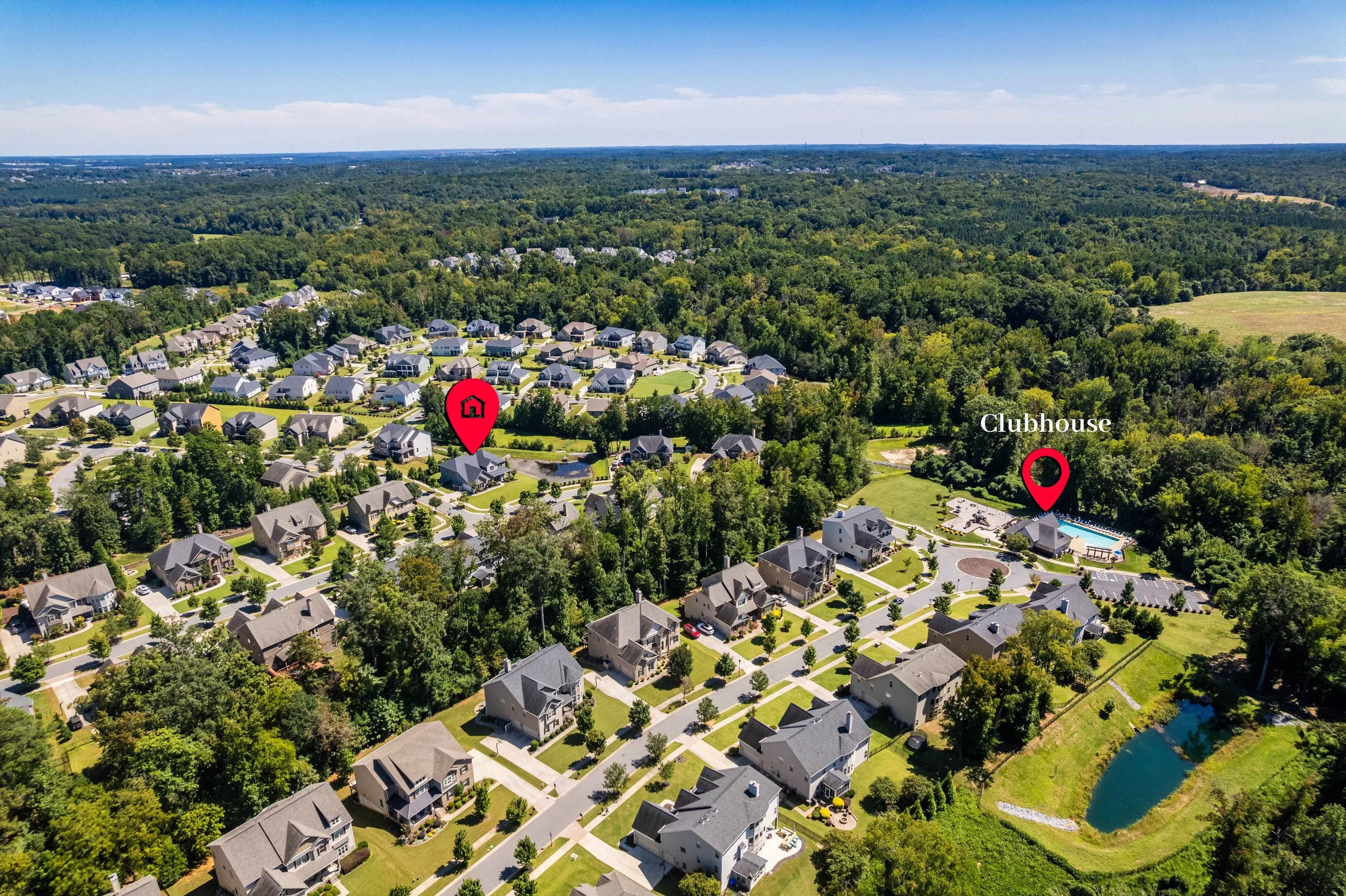 Aerial view of a suburban neighborhood surrounded by trees. Red pins highlight a house and a clubhouse. Bright, sunny day conveys a peaceful tone.