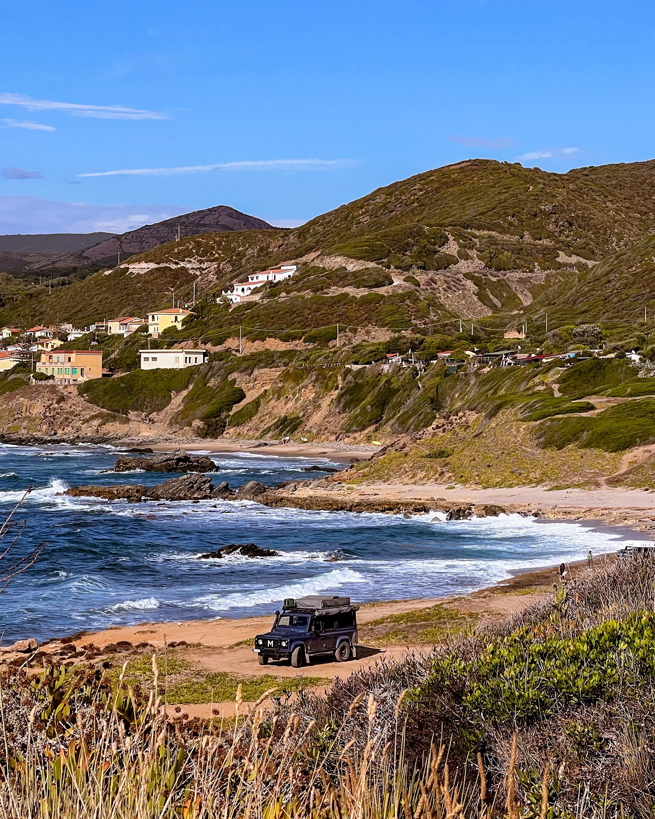 Blauer Land Rover Defender parkt in sardischer Sanddüne.