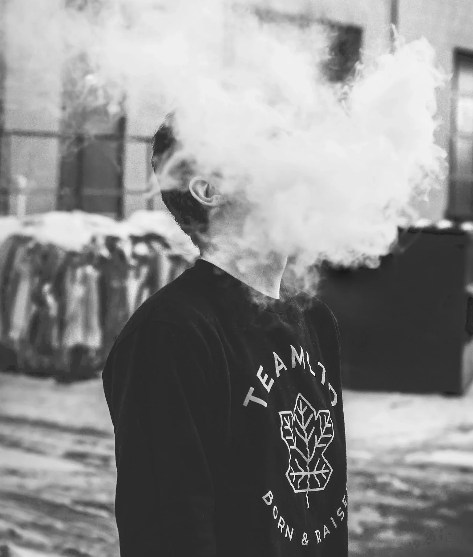 Junger Mann steht im Hinterhof und raucht. Der Rauch verdeckt sein Gesicht.