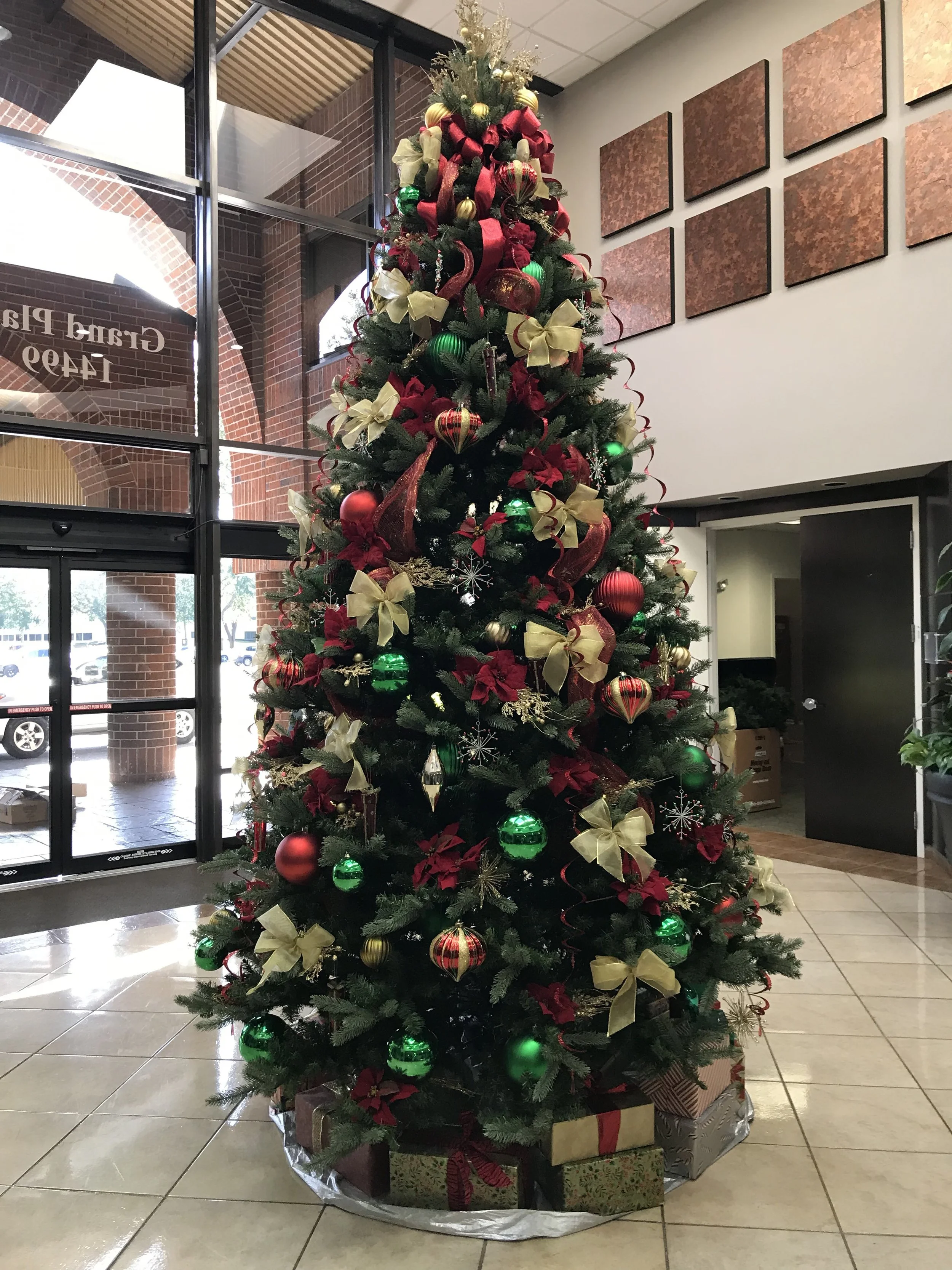 Christmas tree decorated with red, green, and gold ornaments, ribbons, poinsettias, and wrapped presents underneath.