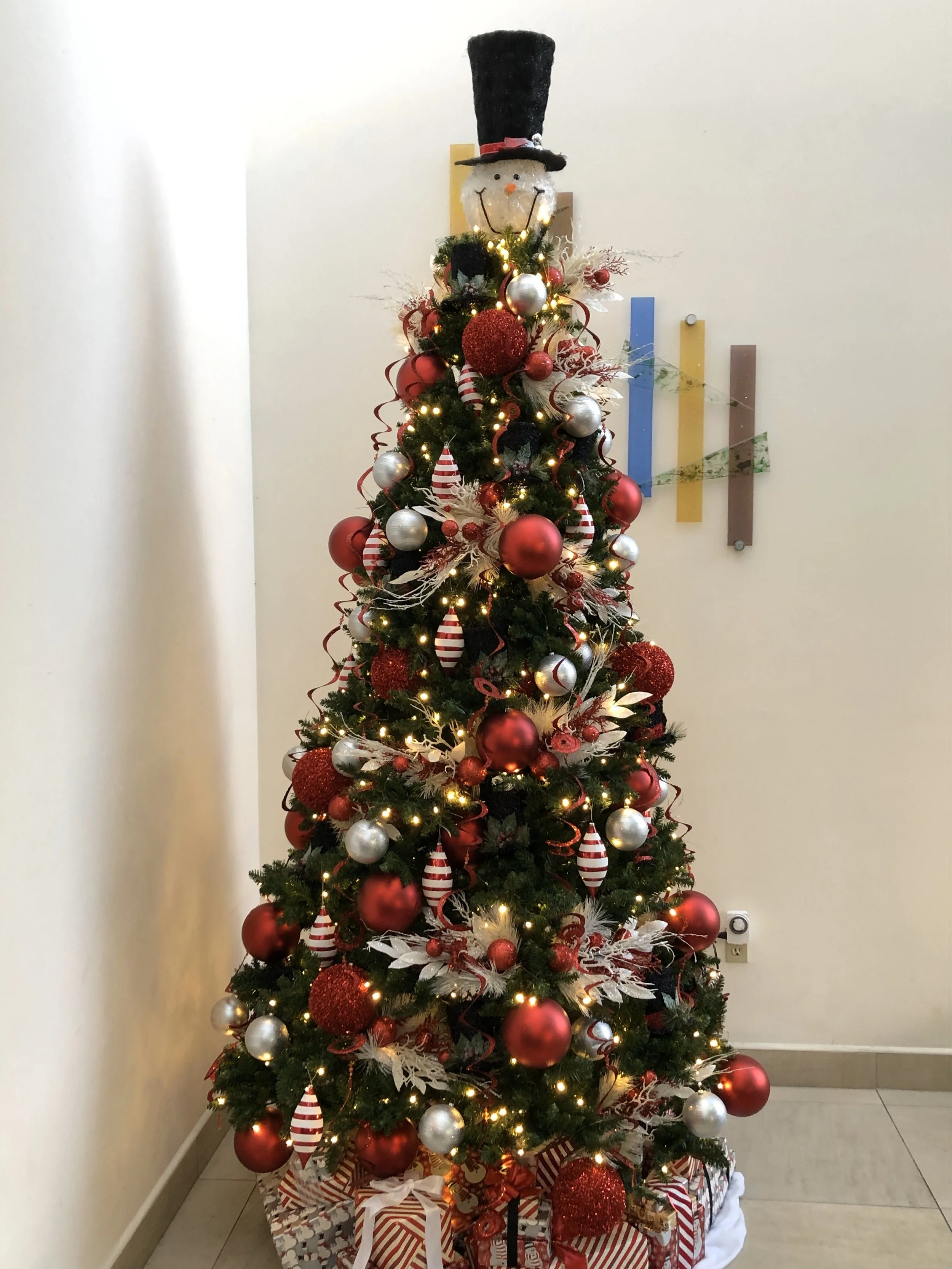 Decorated Christmas tree with red, silver, and white ornaments, ribbons, and a snowman topper
