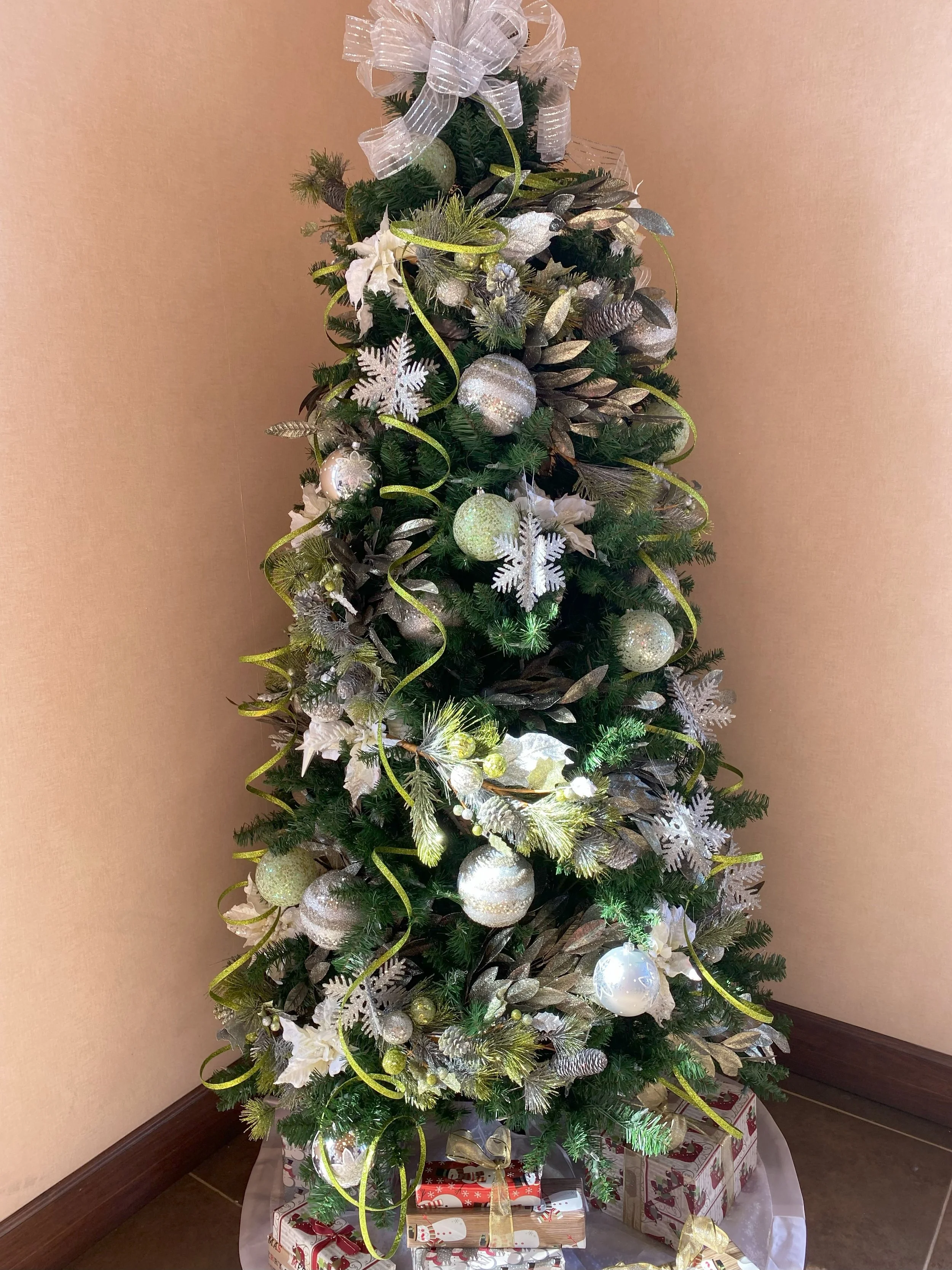 A decorated Christmas tree with white, silver, and gold ornaments, ribbons, and snowflake decorations, with wrapped presents underneath.