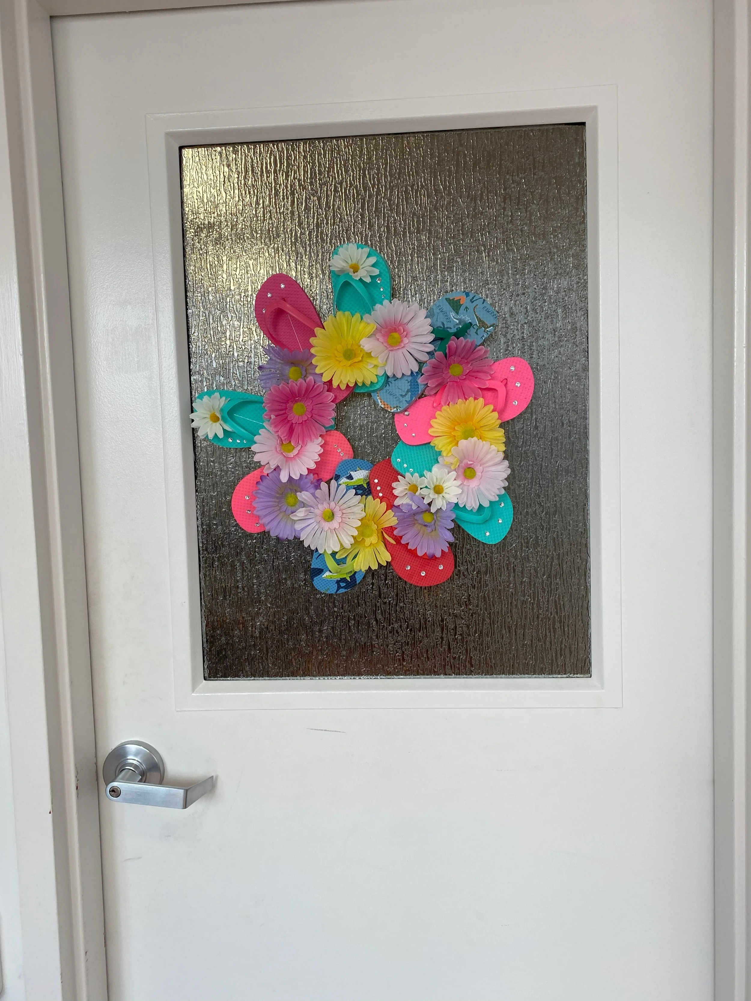 Decorative Easter wreath on a glass door, made of colorful foam eggs and artificial flowers in pink, yellow, purple, and white.