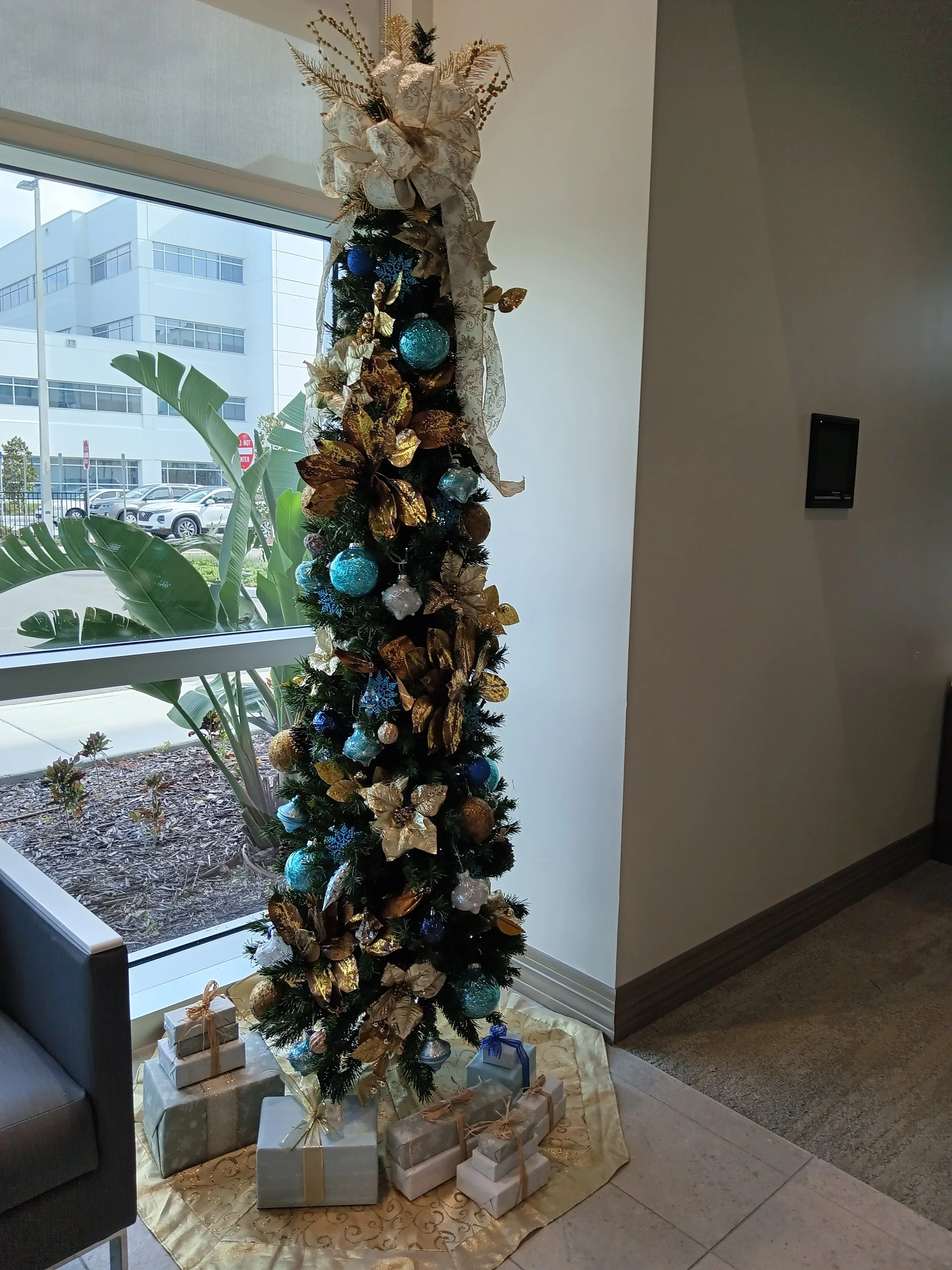 Decorated Christmas tree with gold and blue ornaments and a white gold bow at the top, surrounded by wrapped presents.