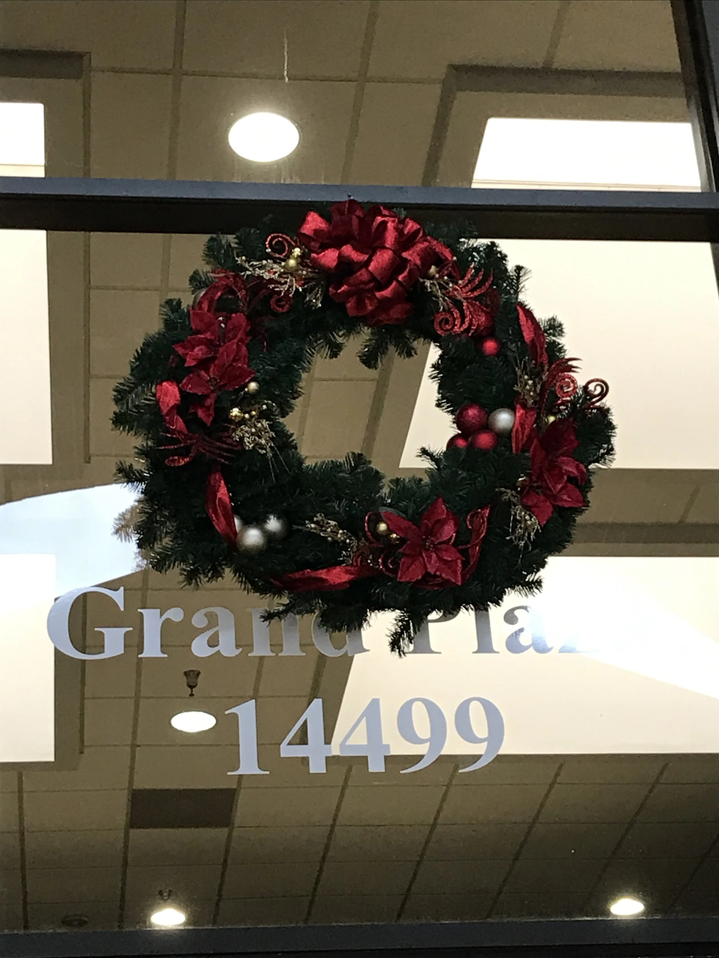 Christmas wreath with red bows, poinsettia flowers, and ornaments hanging on a store window with the text 'Graham Tal 14499'.