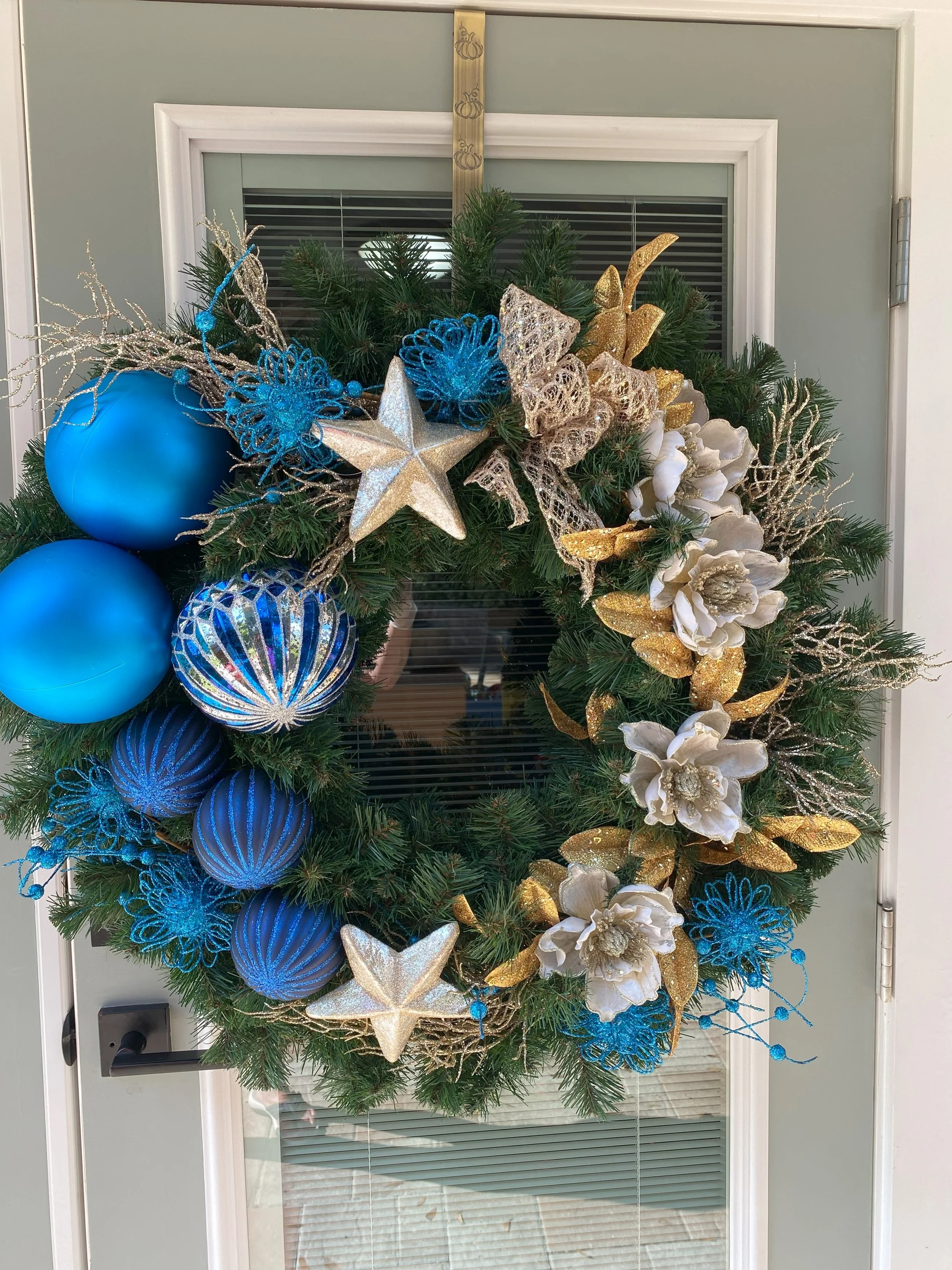 Christmas wreath decorated with blue, gold, and white ornaments, ribbons, and flowers hanging on a door.