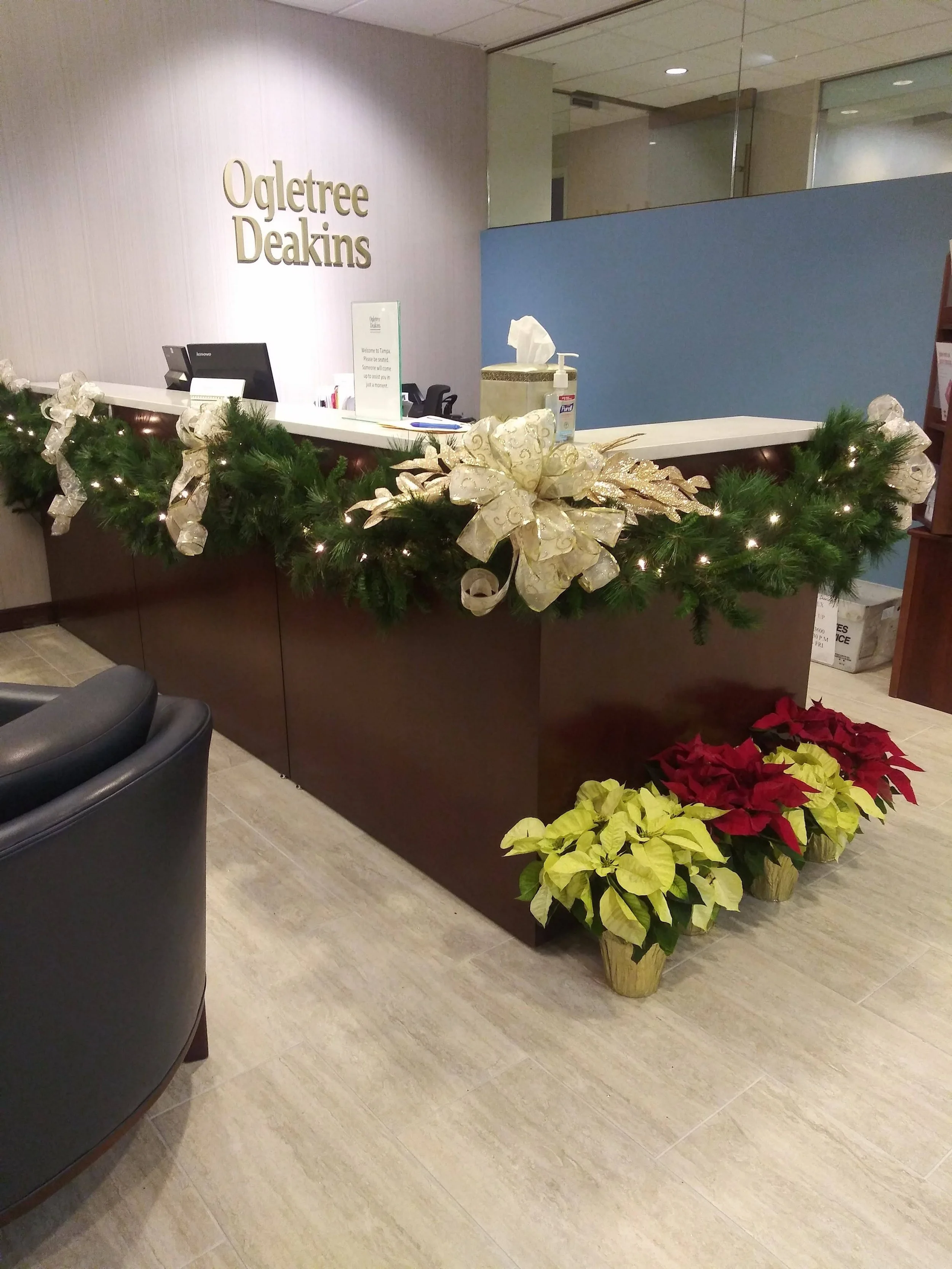 Reception desk decorated with Christmas garland, large gold bow, and poinsettia plants, at Ogletree Deakins law firm.