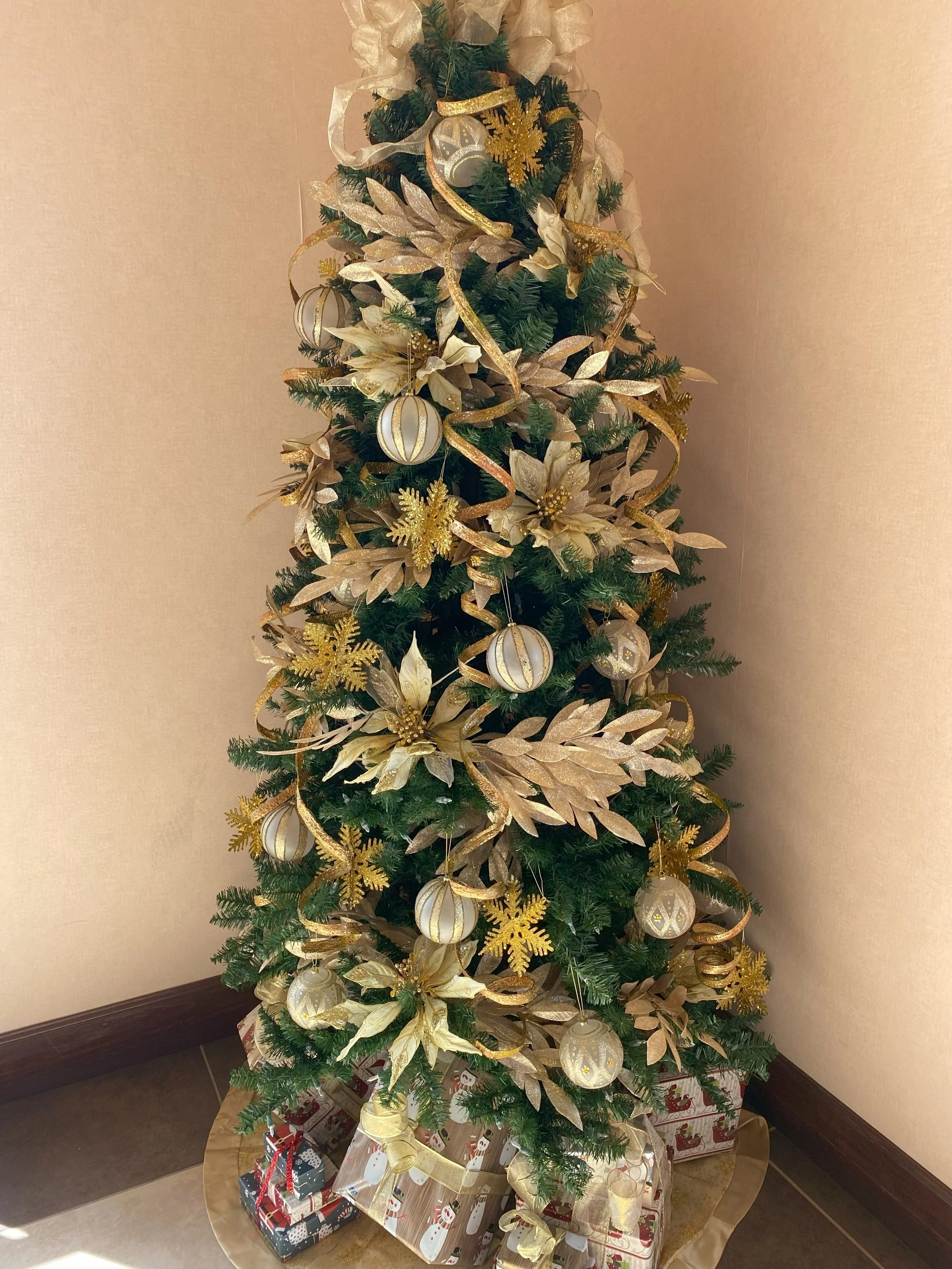 A decorated Christmas tree with gold and white ornaments, poinsettia and snowflake decorations, and wrapped presents at the base.
