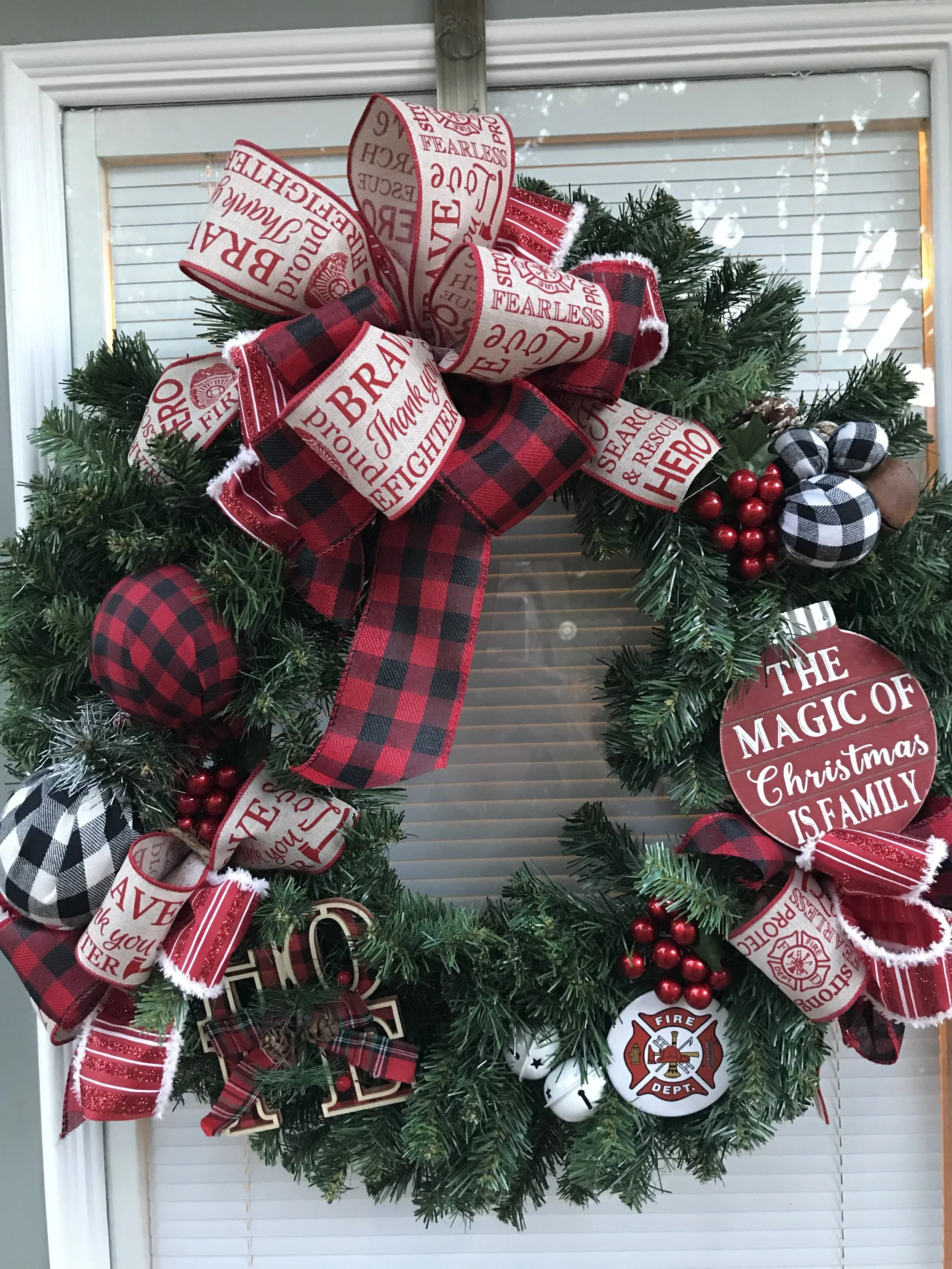 Christmas wreath decorated with red and black plaid ribbons, small ornaments, red berries, and a wooden sign that says 'The magic of Christmas is family'.