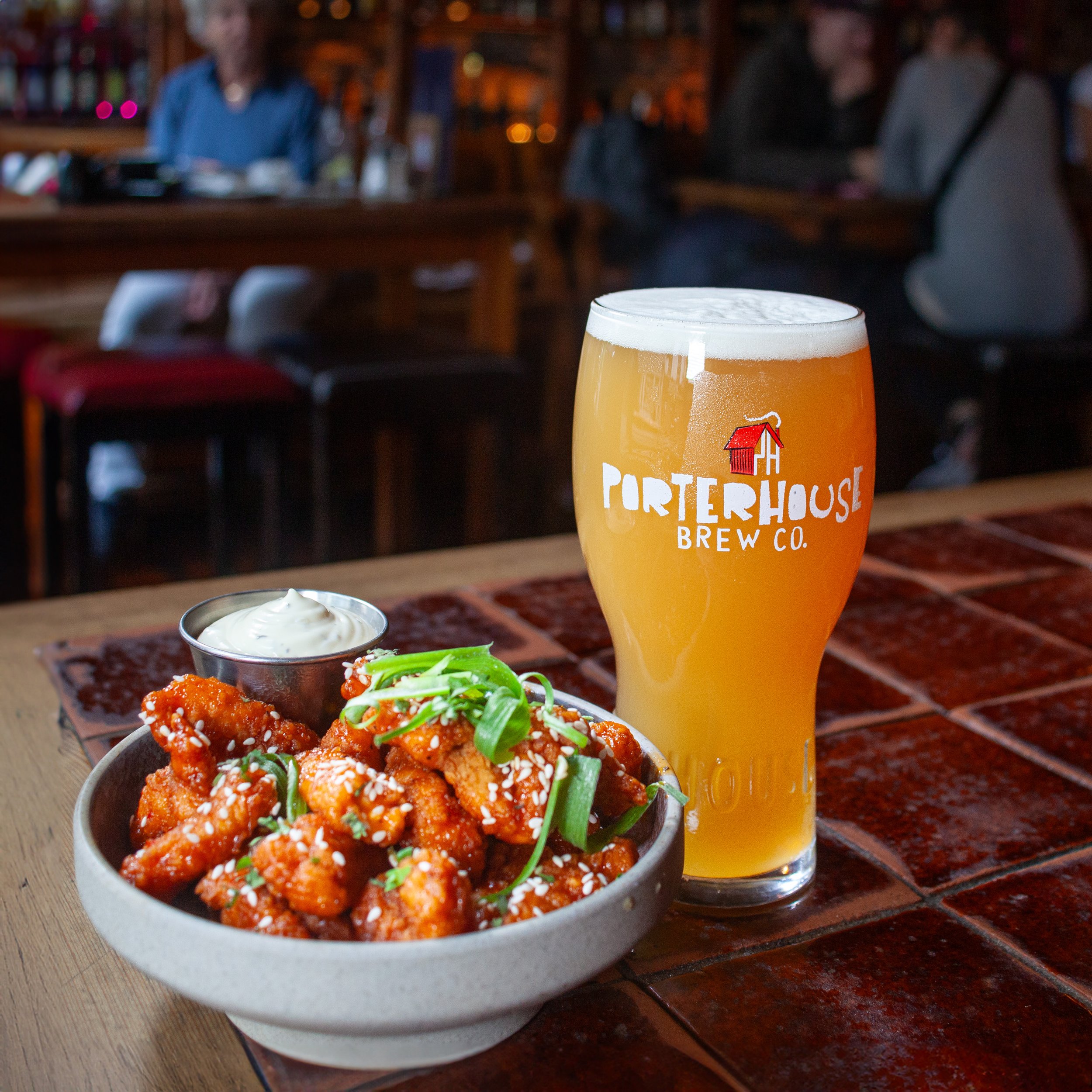 A glass of Porterhouse Brew Co. beer next to a bowl of spicy chicken wings with a side of ranch dressing on a restaurant table.
