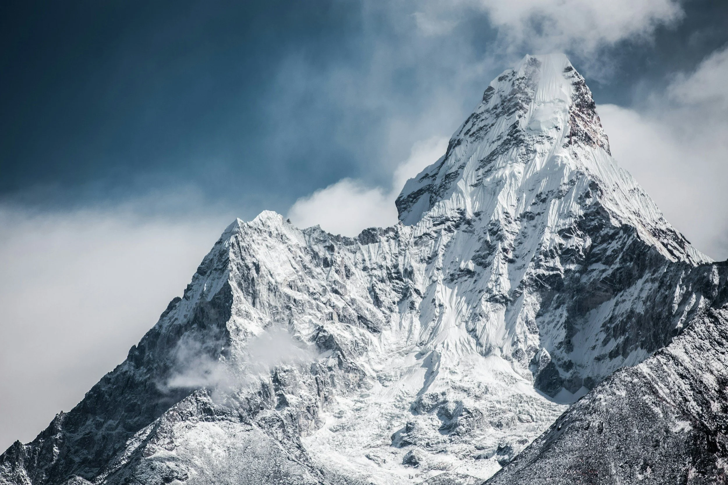 A tall, snow-covered mountain peak with a partly cloudy sky in the background.
