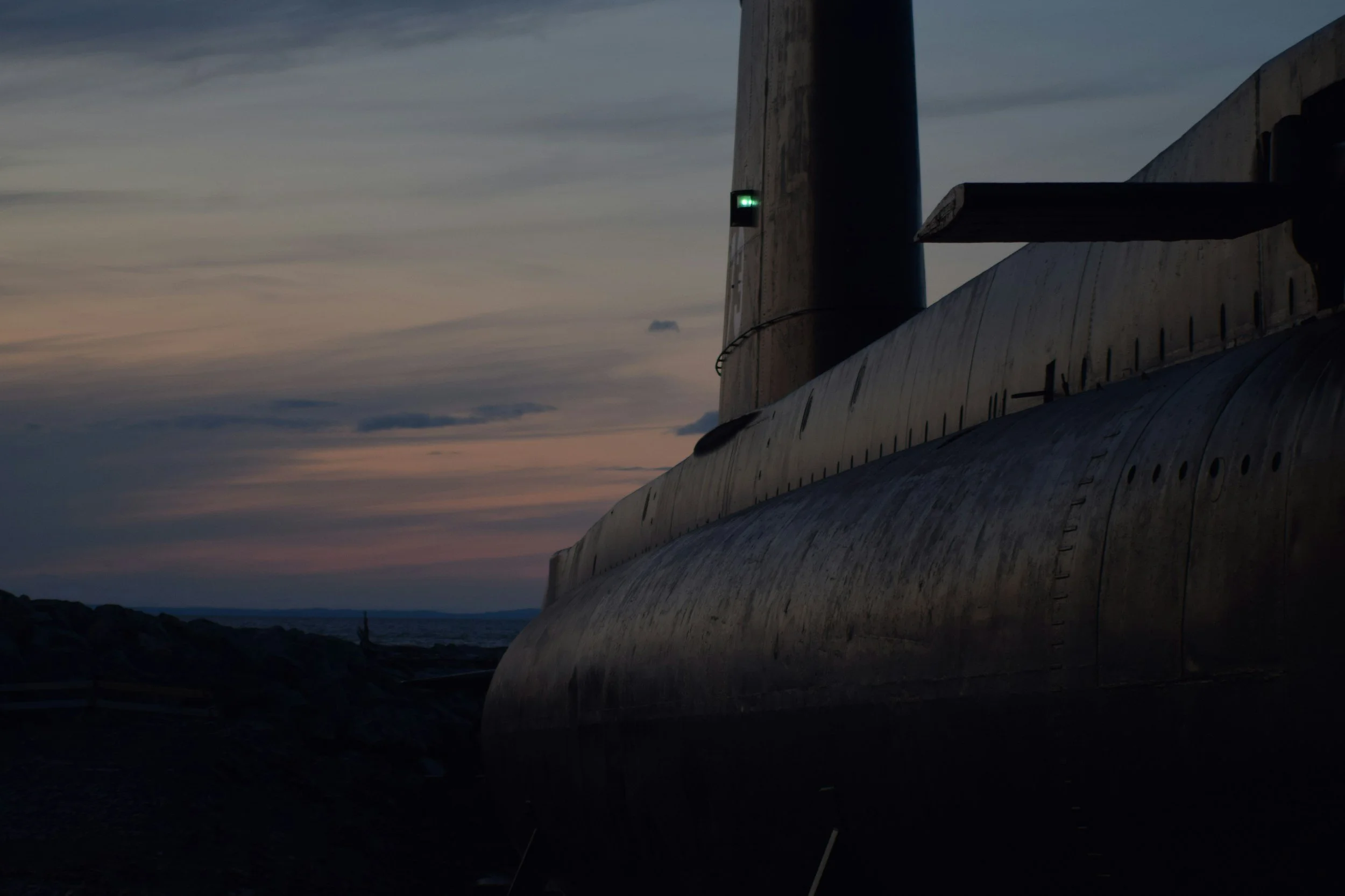Side view of a submarine on a rocky shore at dusk with a partly cloudy sky in the background.
