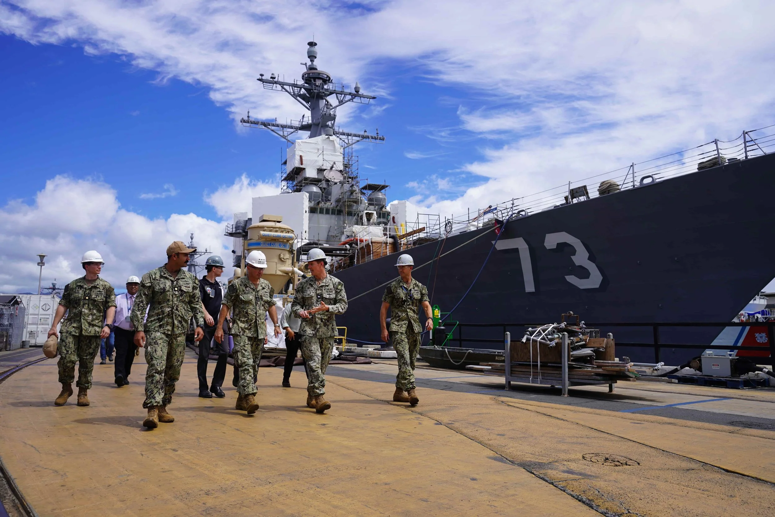 Group of military personnel walking on the dock beside a large naval warship with the number 13 on its side, under partly cloudy sky.