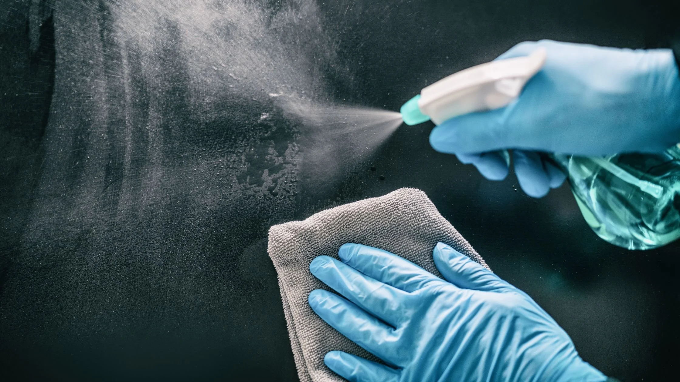 Gloved hands disinfecting a salon or spa surface with spray cleaner and microfiber cloth