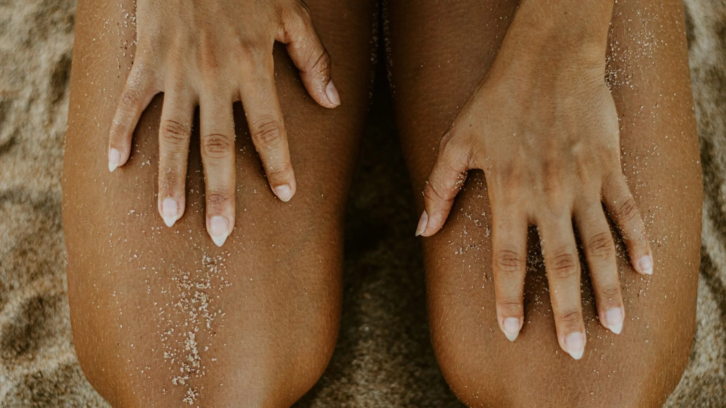 Closeup of legs and knees of a woman kneeling on the sand placing her hands on her legs