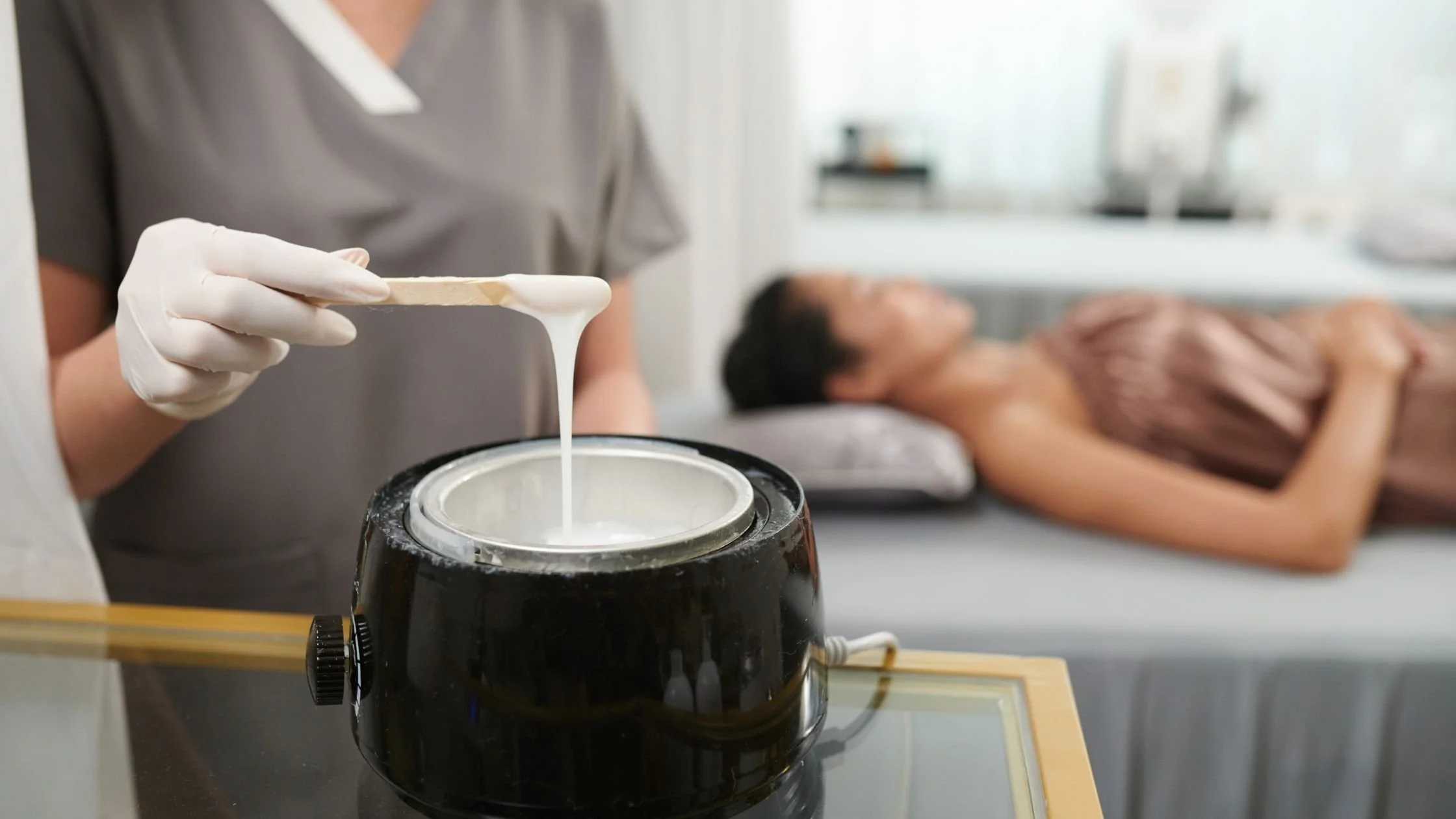 Esthetician holding a waxing applicator over a wax warmer during a spa treatment