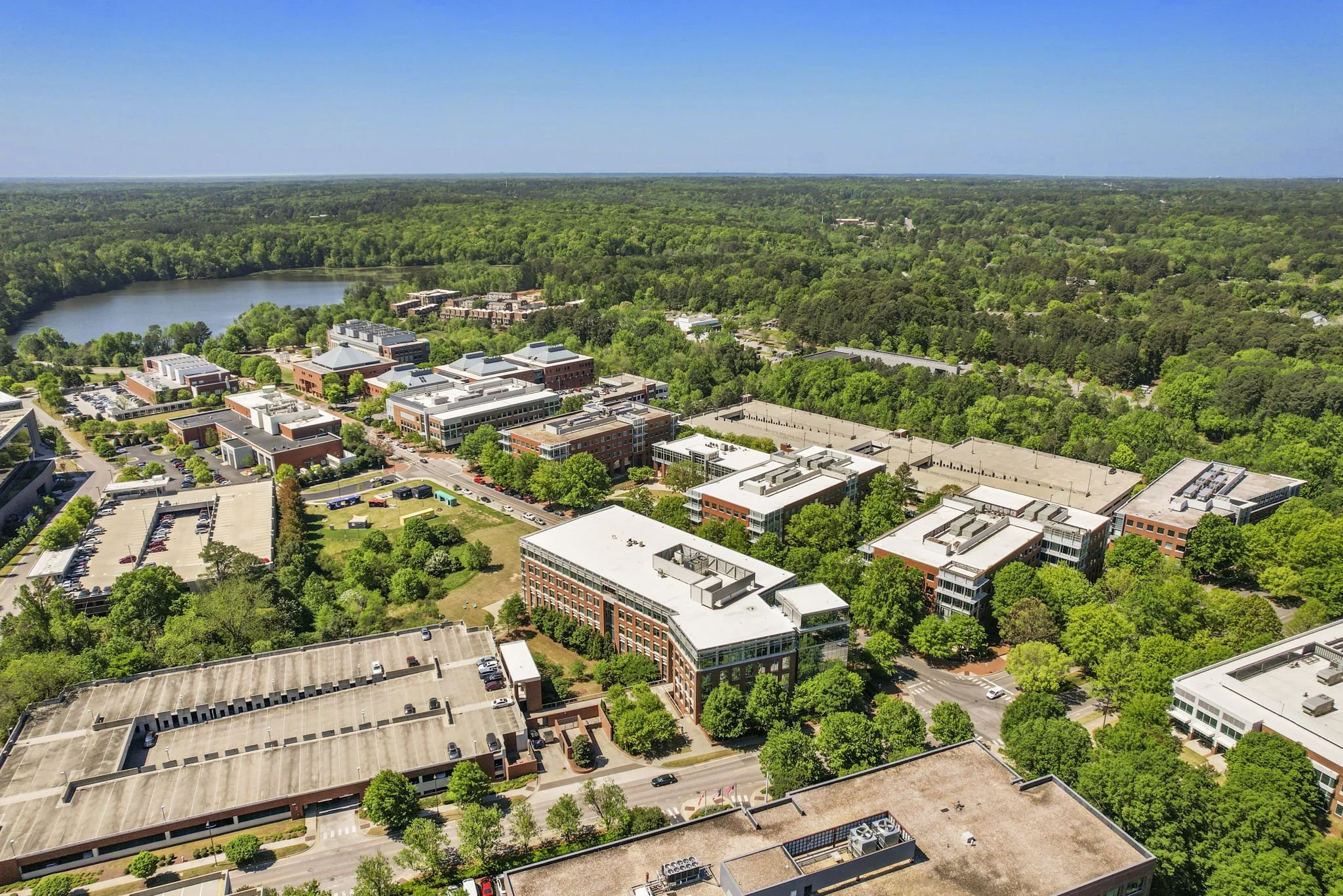 Aerial view of a college campus surrounded by green trees and a body of water in the background.