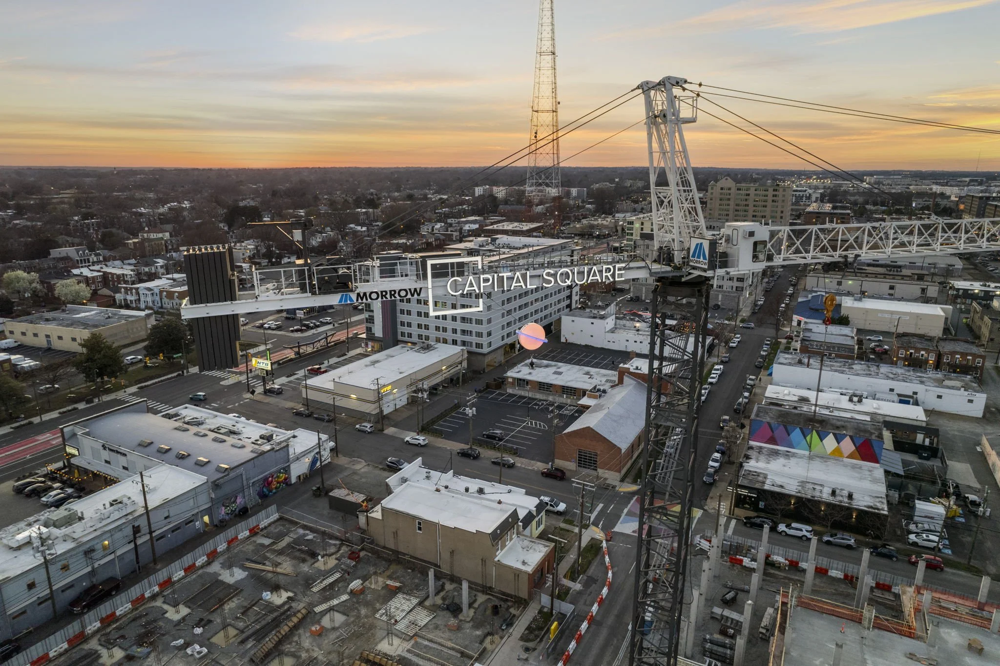 An aerial view of Capital Square at dusk with a construction crane, city streets, buildings, and colorful murals.