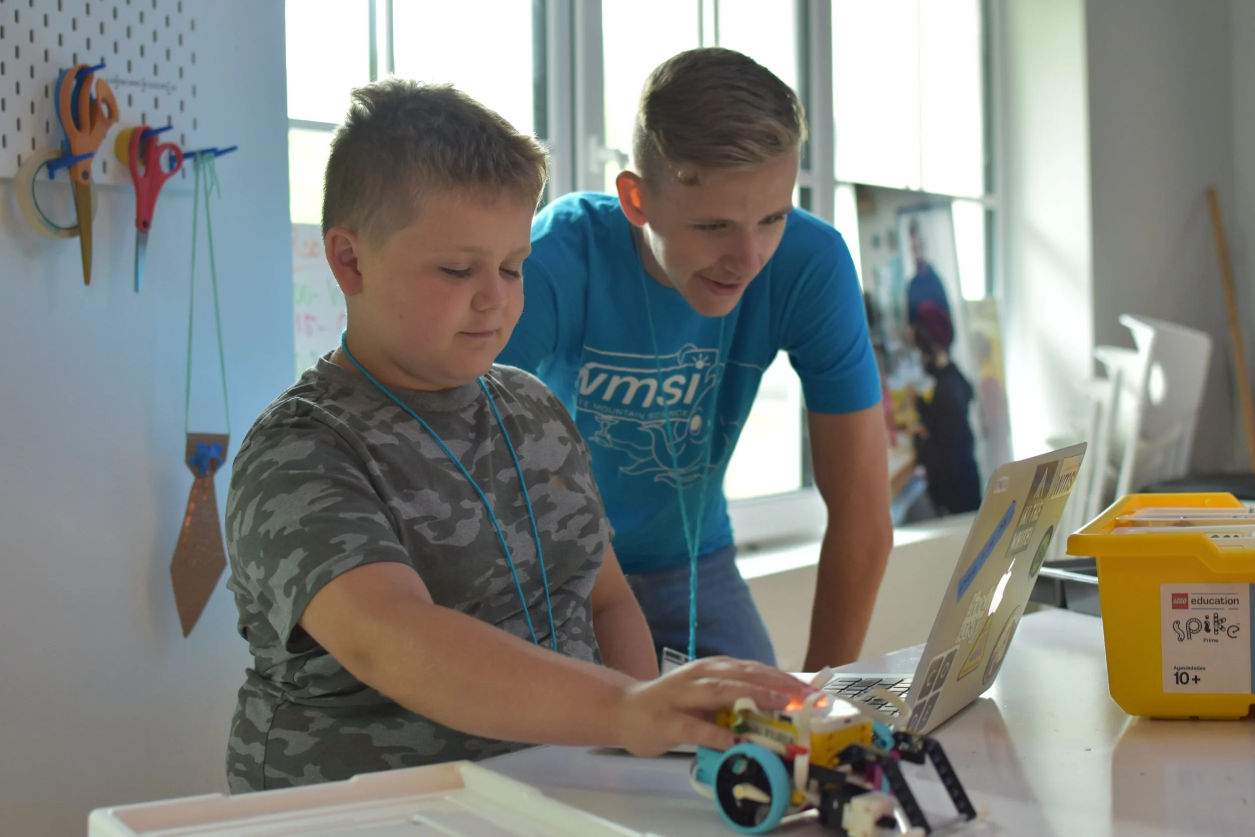 A young boy working on a robotics project, with a man assisting him, at a table in a classroom.