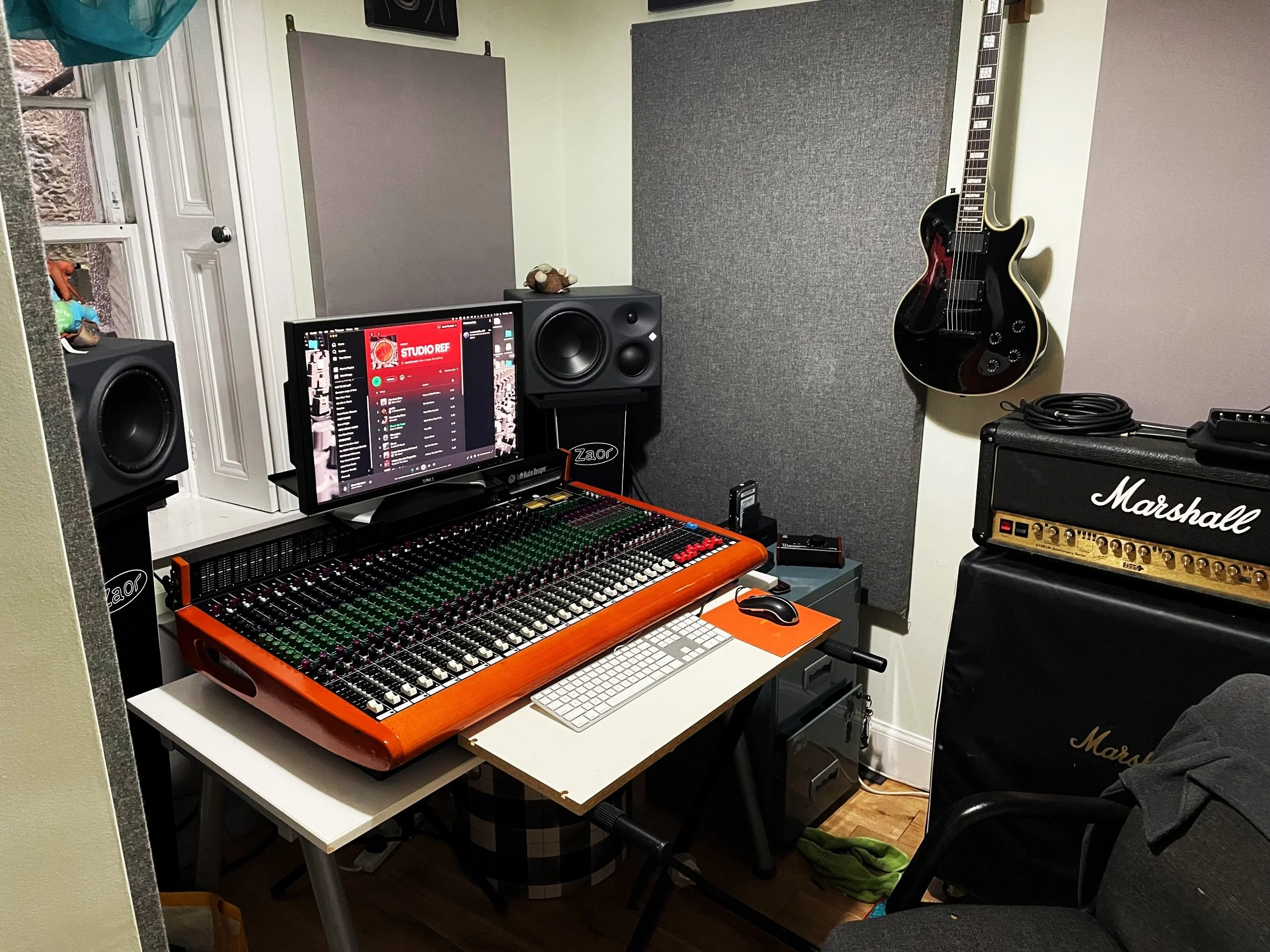 Private recording studio with mixing console, speakers, computer monitor, electric guitar on wall, and Marshall amplifier.