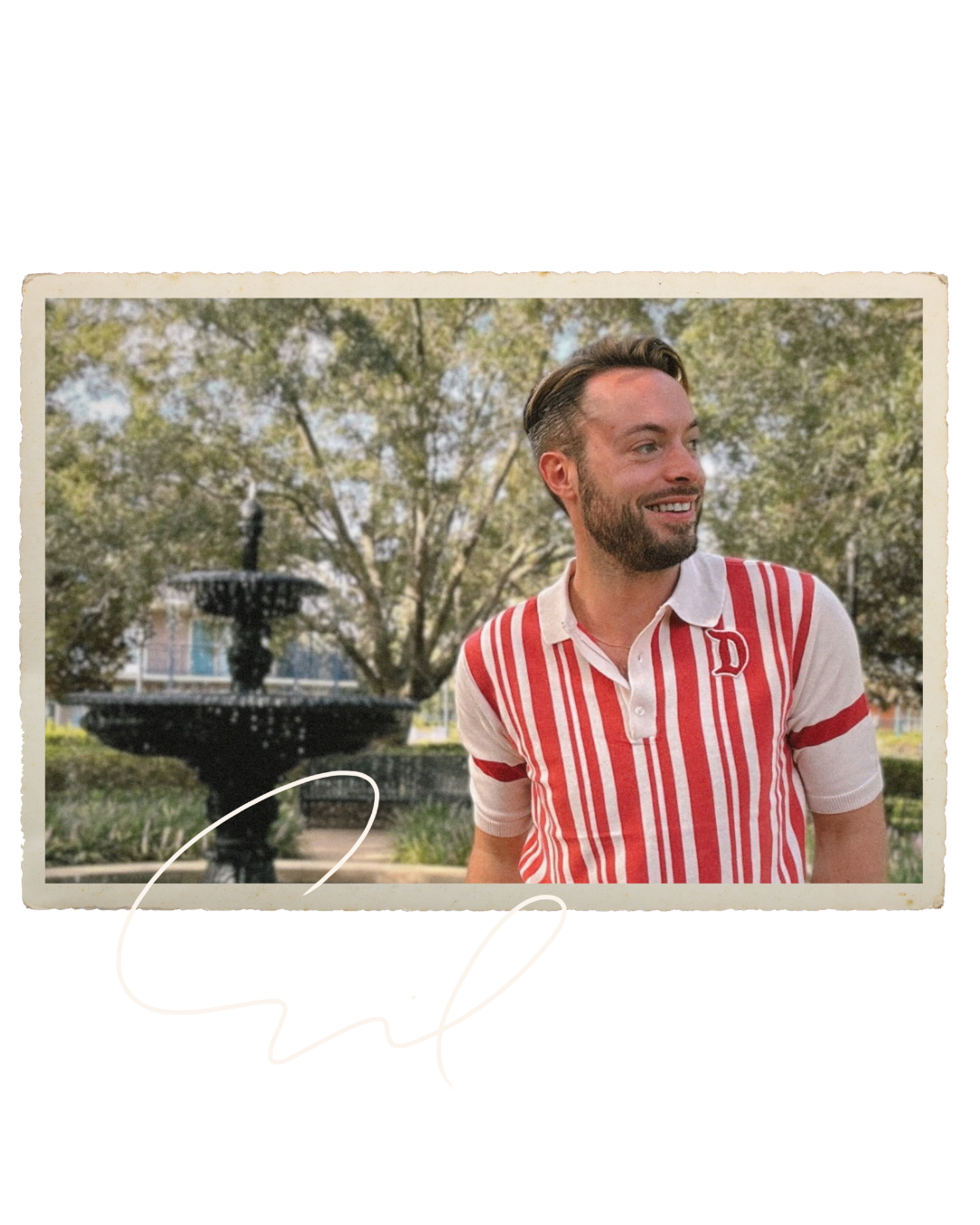 A man with a beard and styled hair smiling outdoors, a personal stylist wearing a red and white striped polo shirt, standing in front of a fountain and trees.