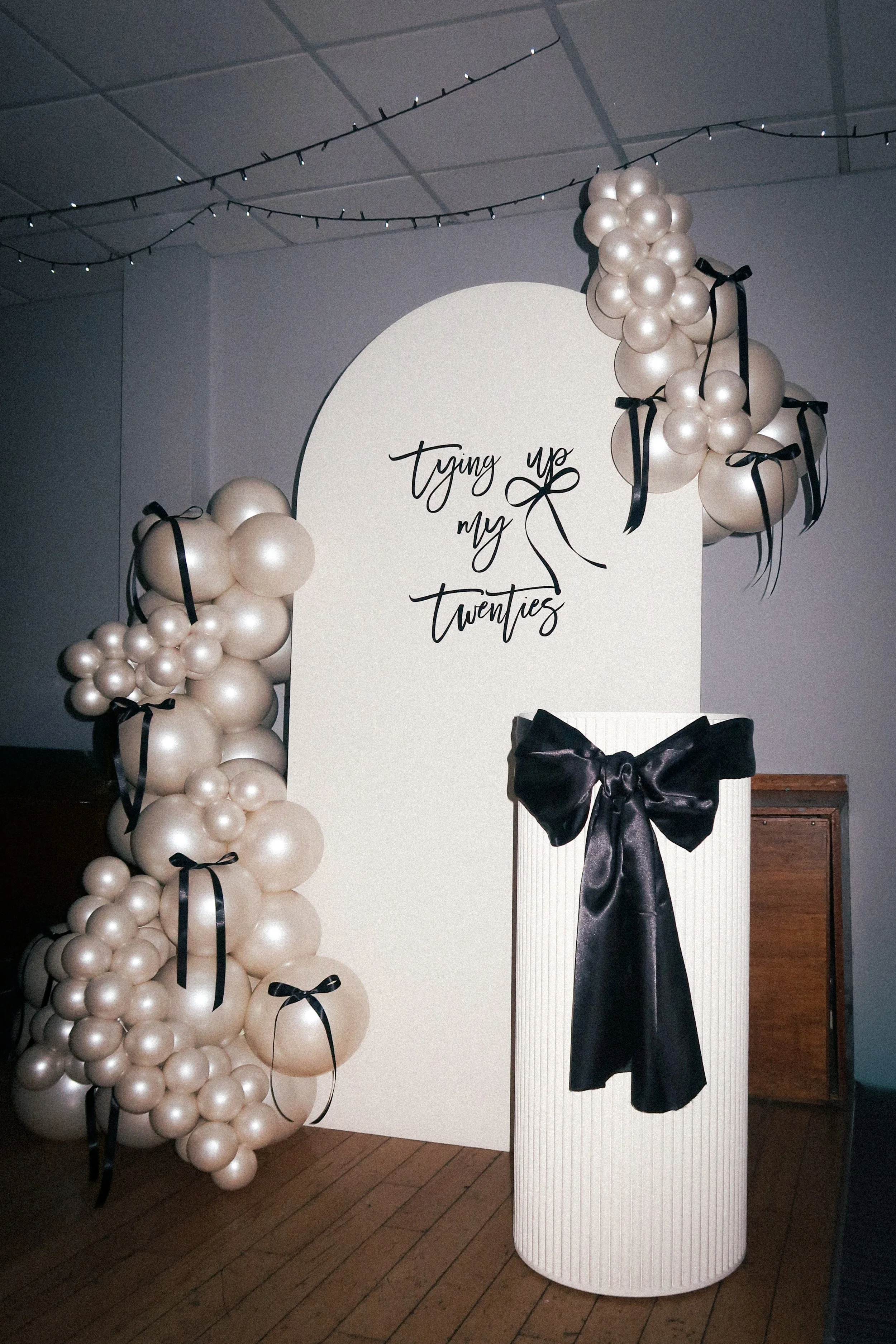 Decorative backdrop with balloon arrangements and a sign that reads "tying up my twenties" for a 20th birthday celebration.