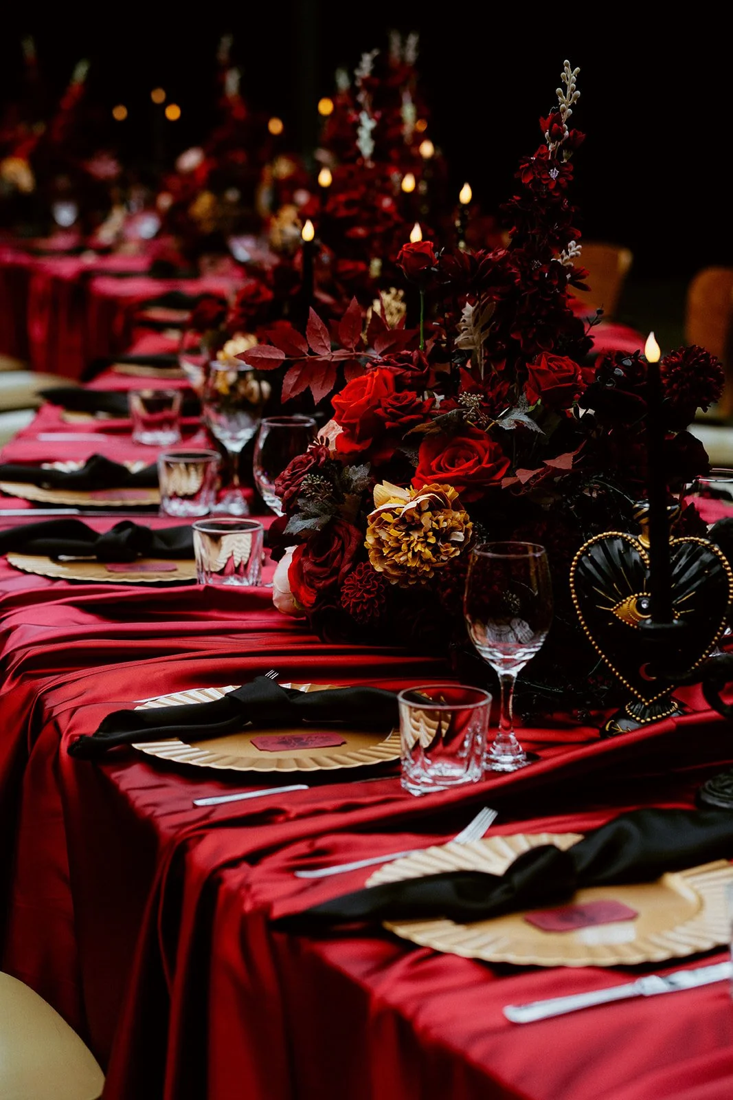 Serpentine wedding reception table styled by Cherry on Pop at BAaD Glasgow, featuring rich red fabric draping, dark romantic faux floral centrepieces, black napkins and statement table décor.
