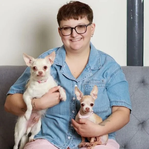 short haired woman sits on couch holding 2 chihuahuas