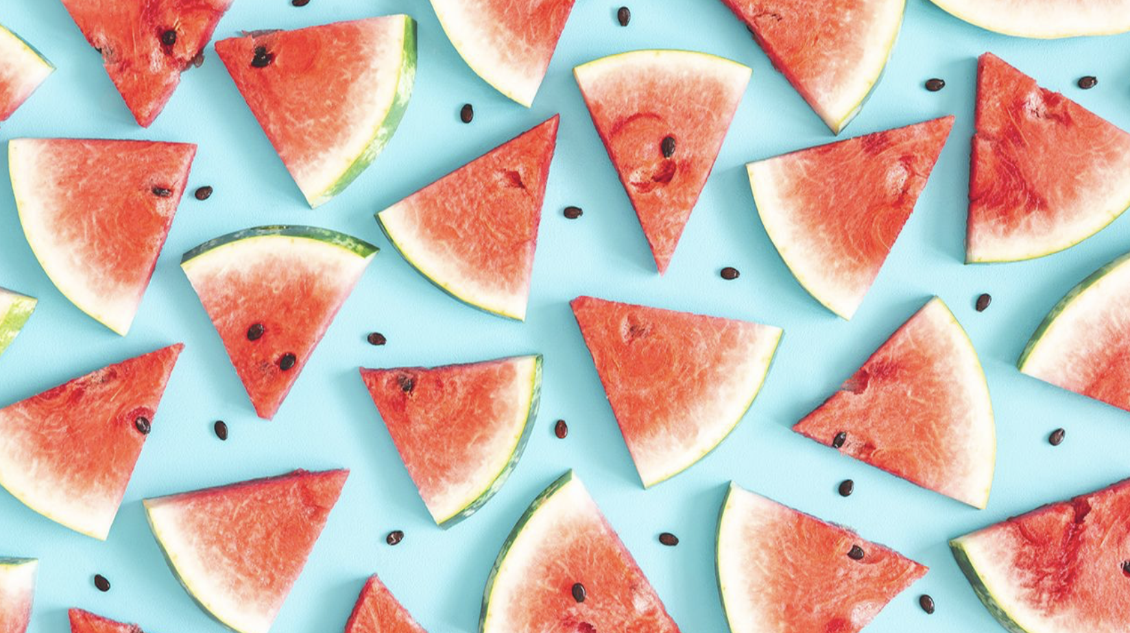 Slices of watermelong and black watermelon seeds scattered between slices all on a light blue background