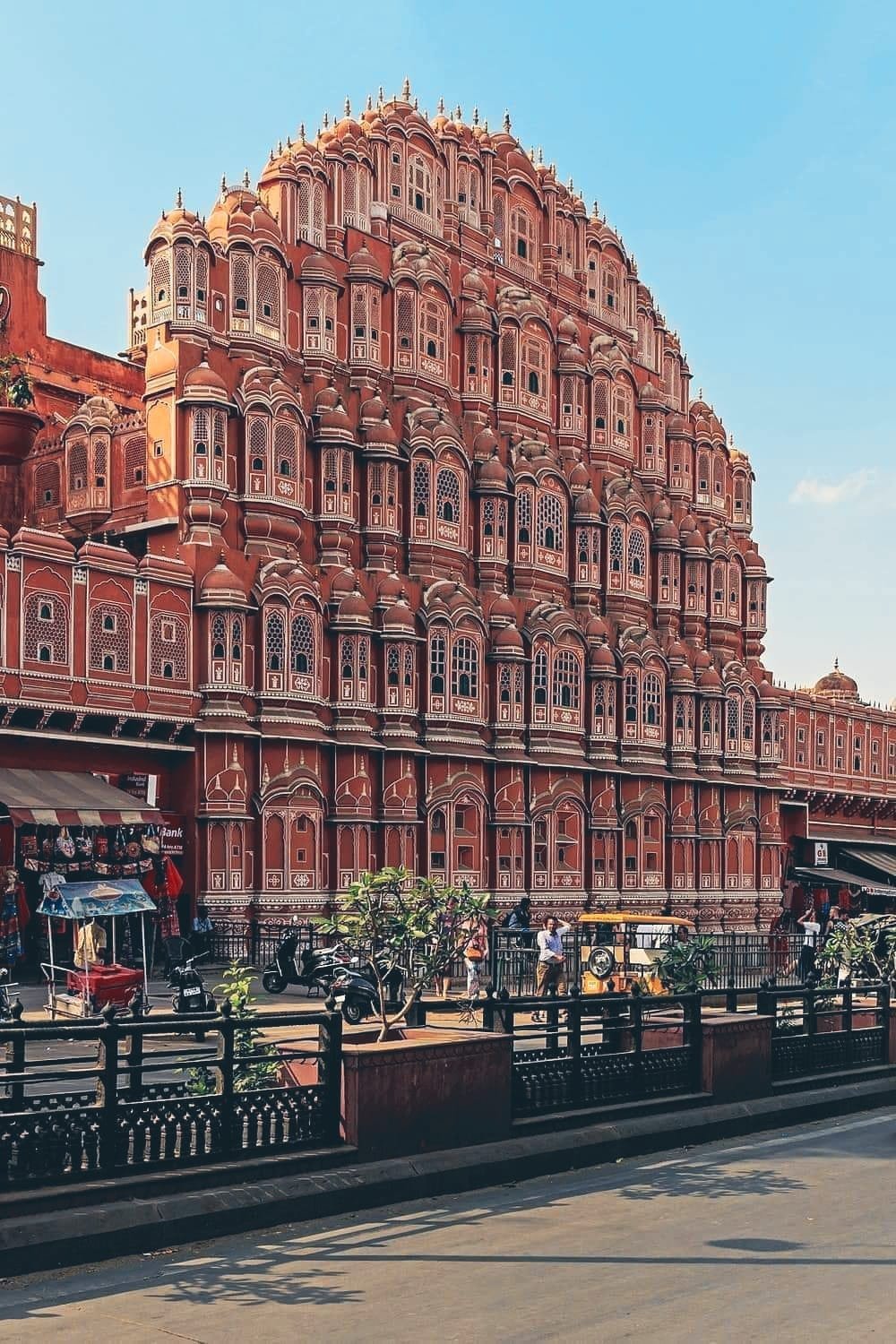 The Hawa Mahal, a pink sandstone palace in Jaipur, India, with intricate lattice work and multiple small windows, seen against a clear blue sky.