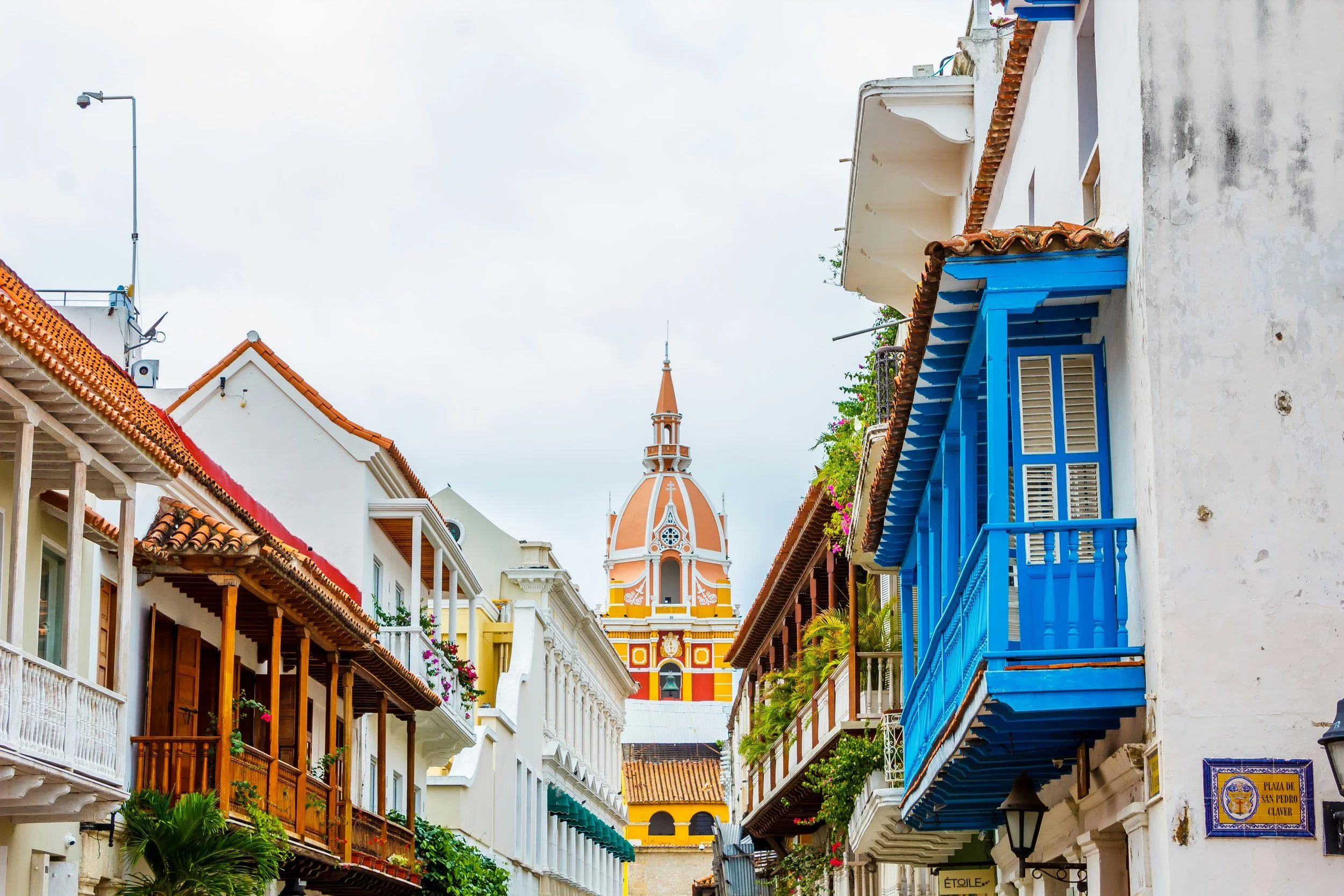 Colorful buildings with wooden balconies, a church with a orange and white dome in the background, and a cloudy sky.