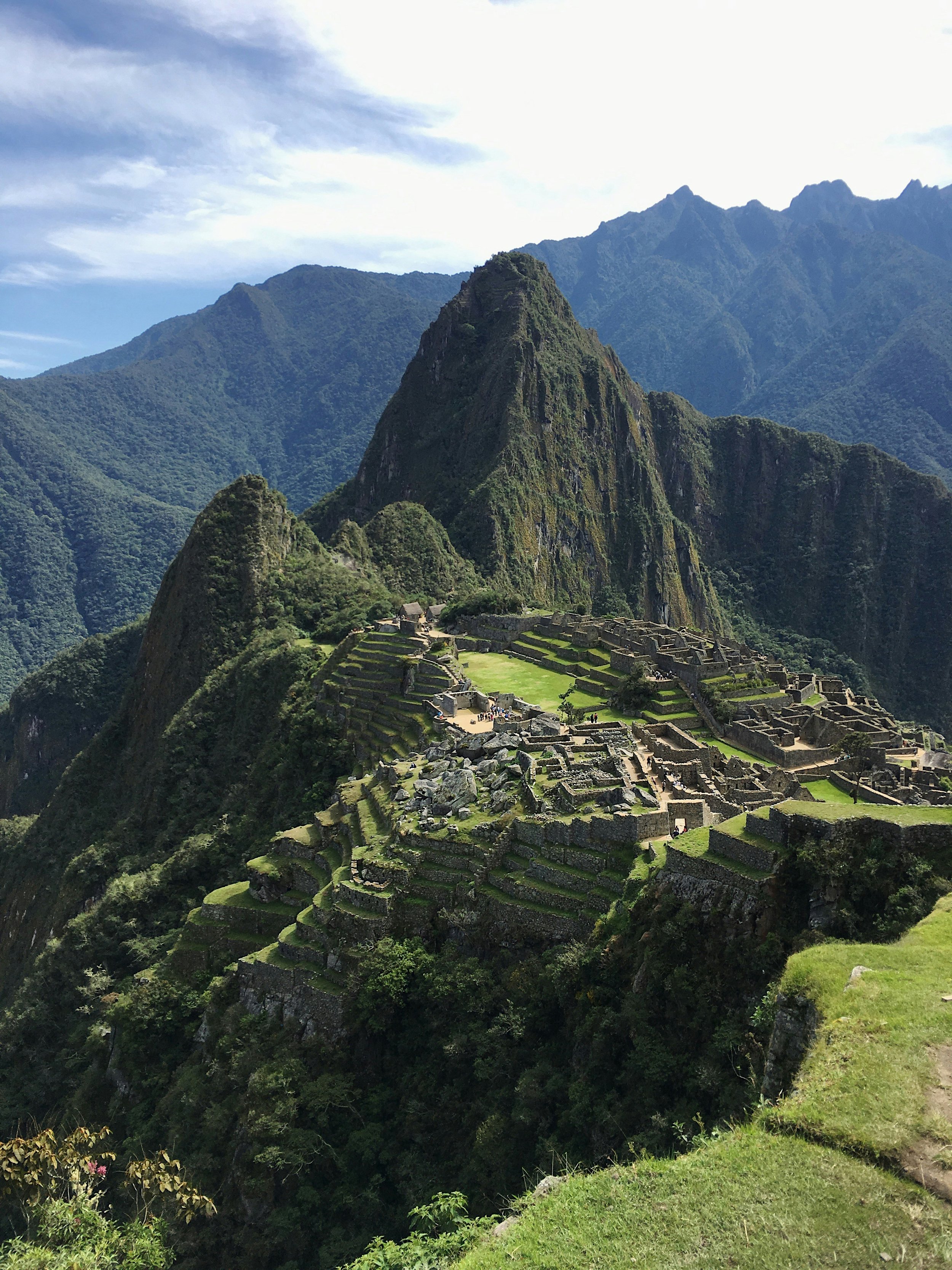 View of Machu Picchu, an ancient Incan city, nestled in the mountains with terraced fields and stone buildings under a blue sky.