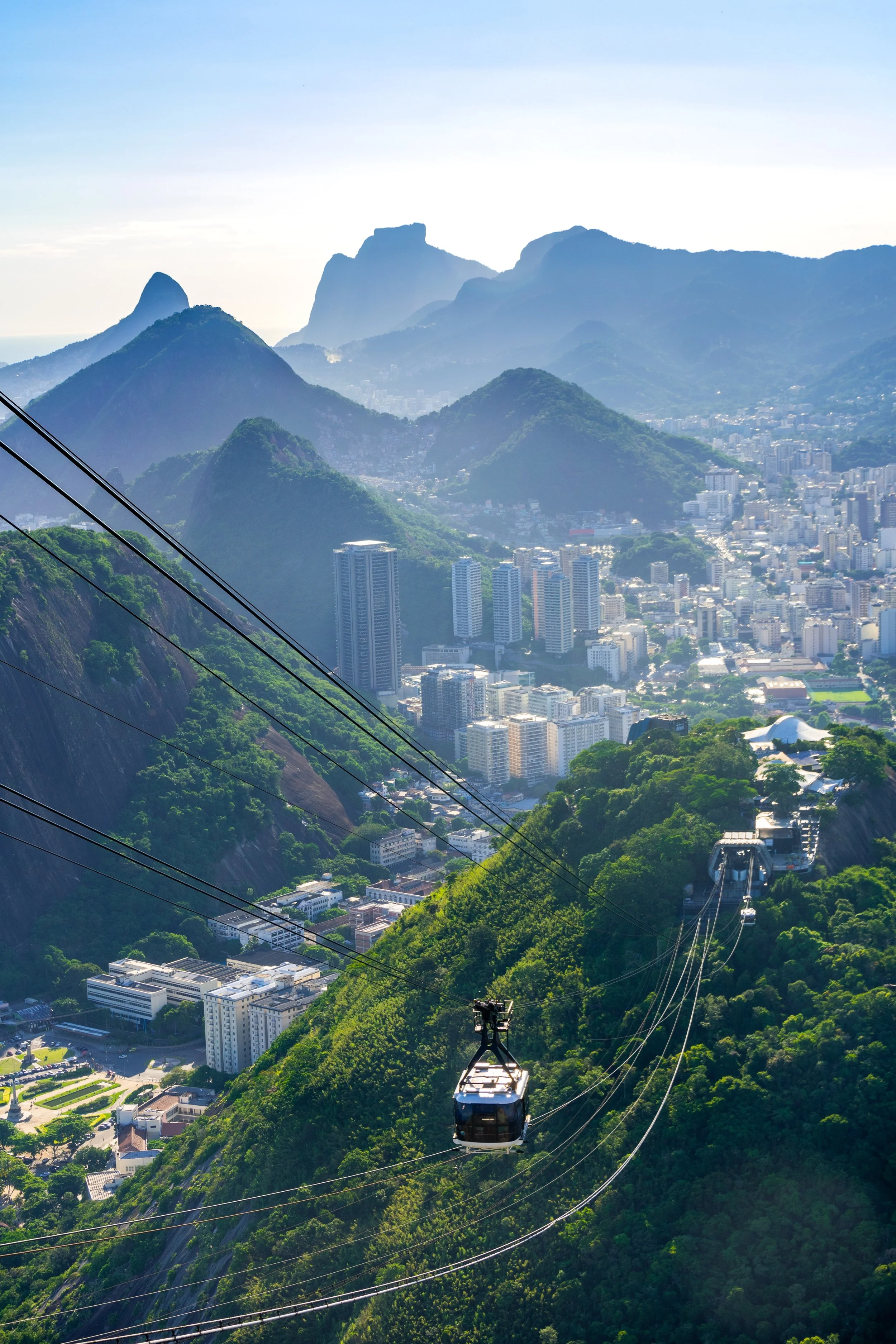 Cable cars traveling over lush green mountains with a cityscape and mountains in the background.