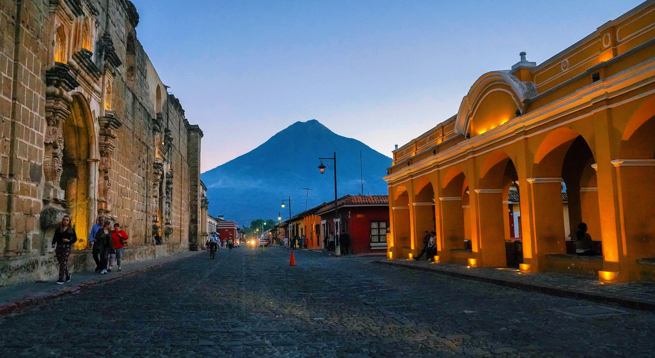 A cobblestone street at dusk with historic buildings on both sides and a mountain in the background.