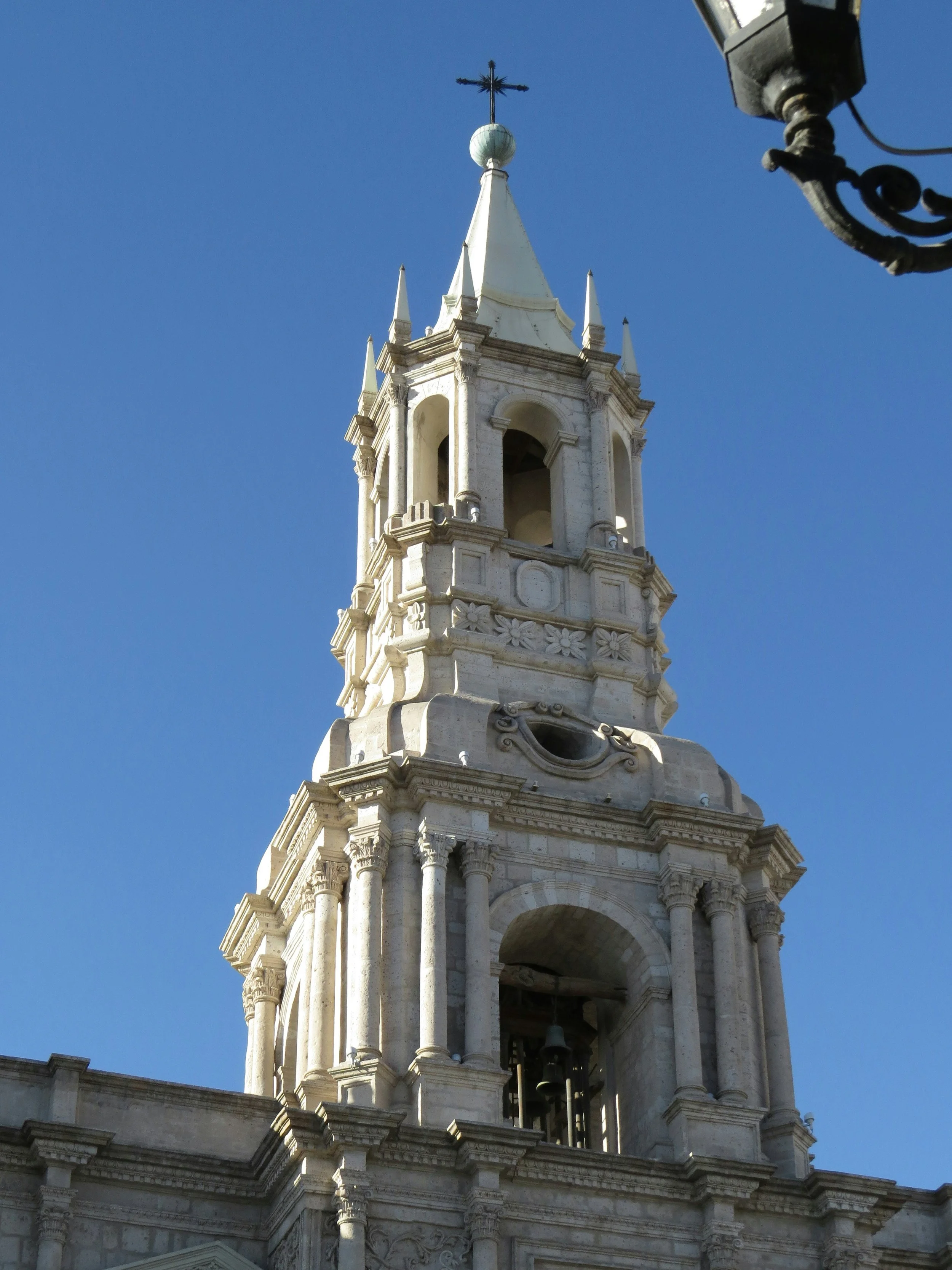 A tall white church tower with a cross on top against a clear blue sky.