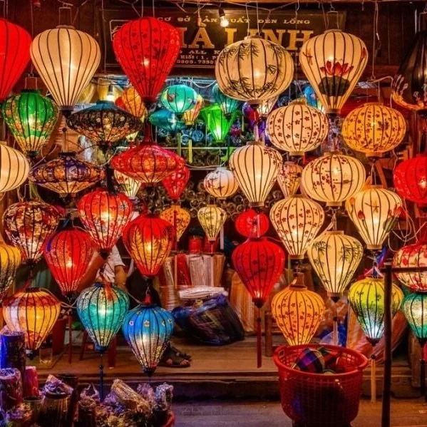 A vibrant display of colorful hanging lanterns in a shop, including red, yellow, green, blue, and orange lanterns with various patterns.