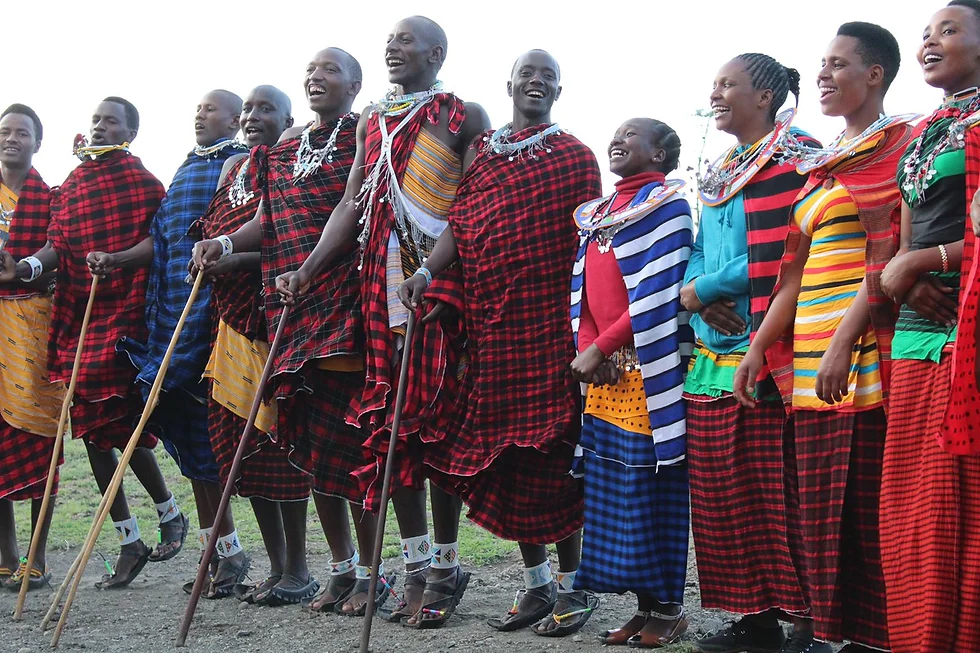 Group of Maasai women dressed in colorful traditional clothing and jewelry, standing outdoors and smiling.