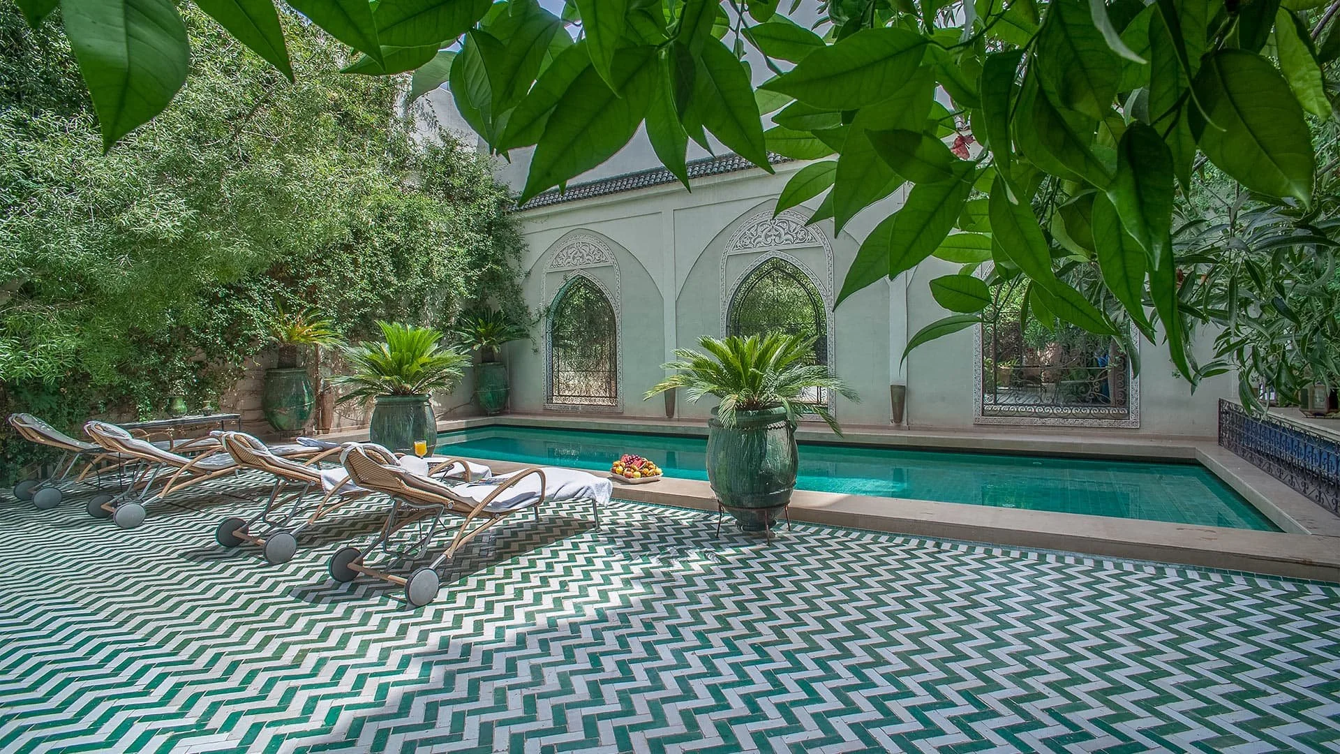 Luxurious indoor pool area surrounded by lush greenery, with sun loungers and decorative potted plants.