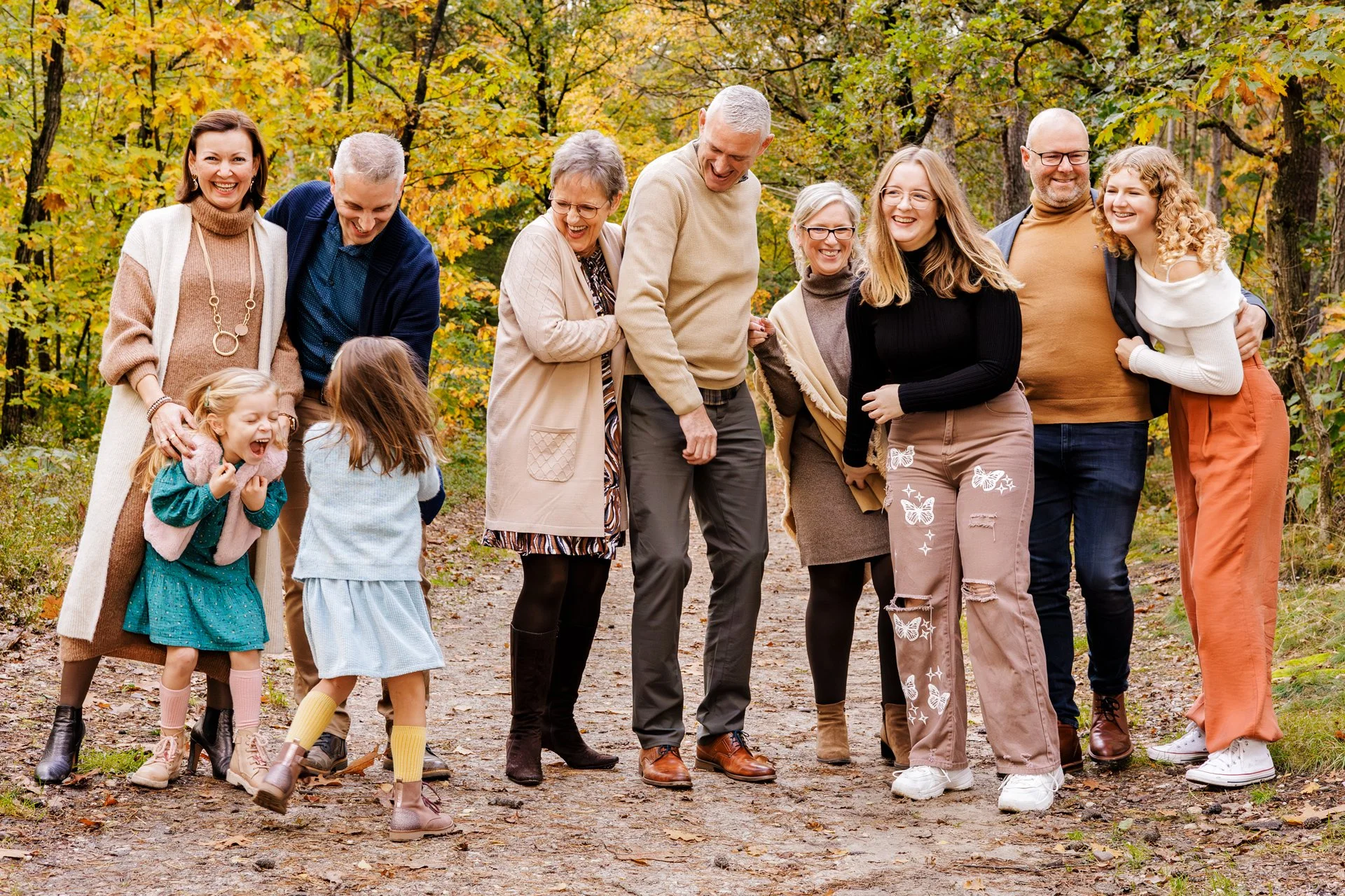 Family and friends enjoying autumn walk in the woods, laughing and smiling, surrounded by fall foliage.
