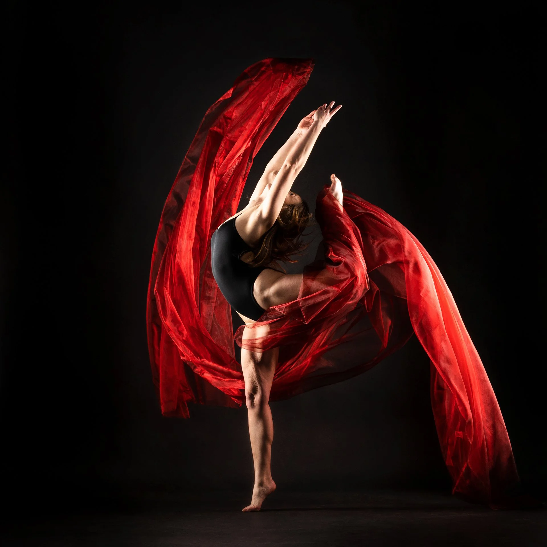 A female gymnast with a flowing red fabric against a dark background.