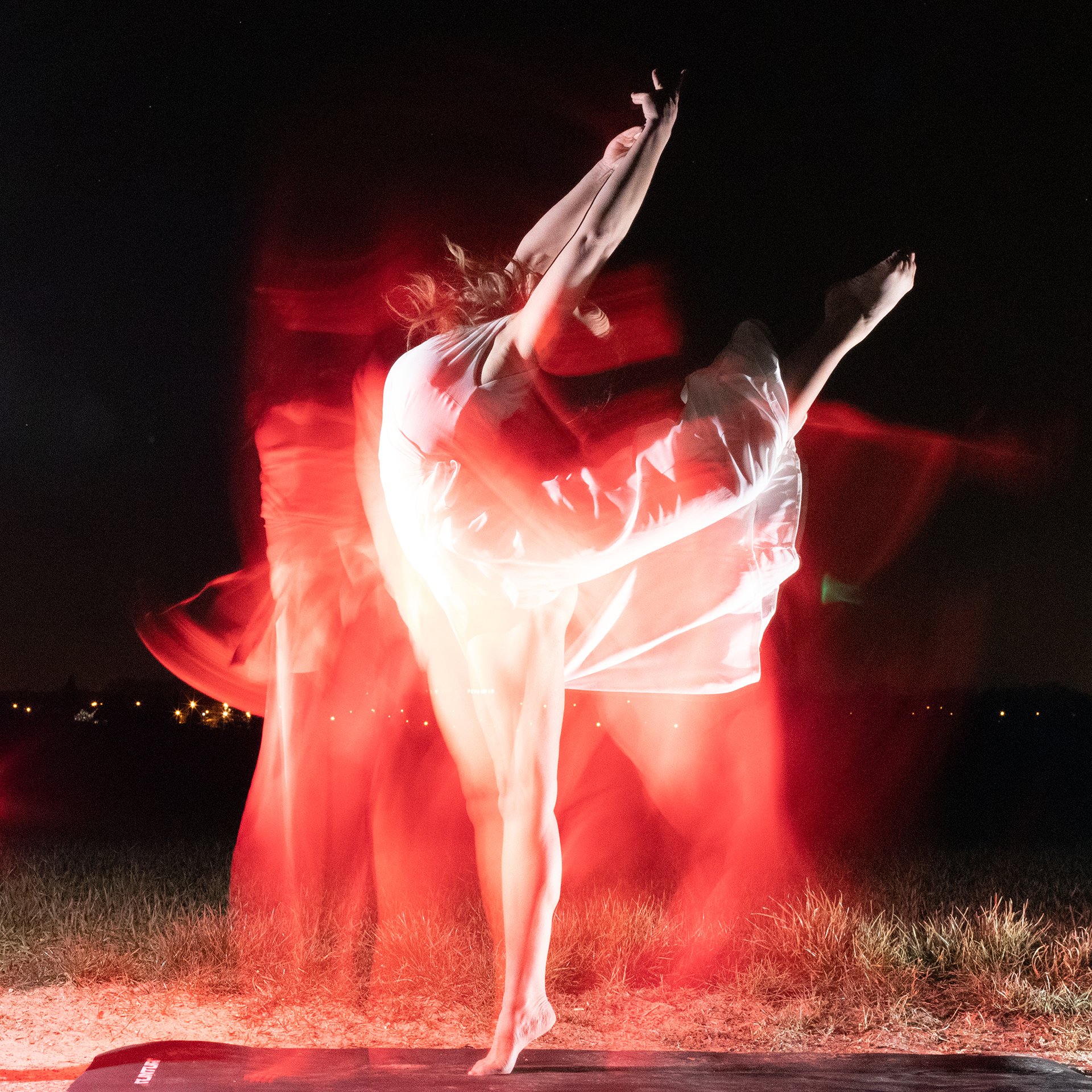 Person dancing outdoors at night, illuminated with red light, captured with long exposure showing motion blur.