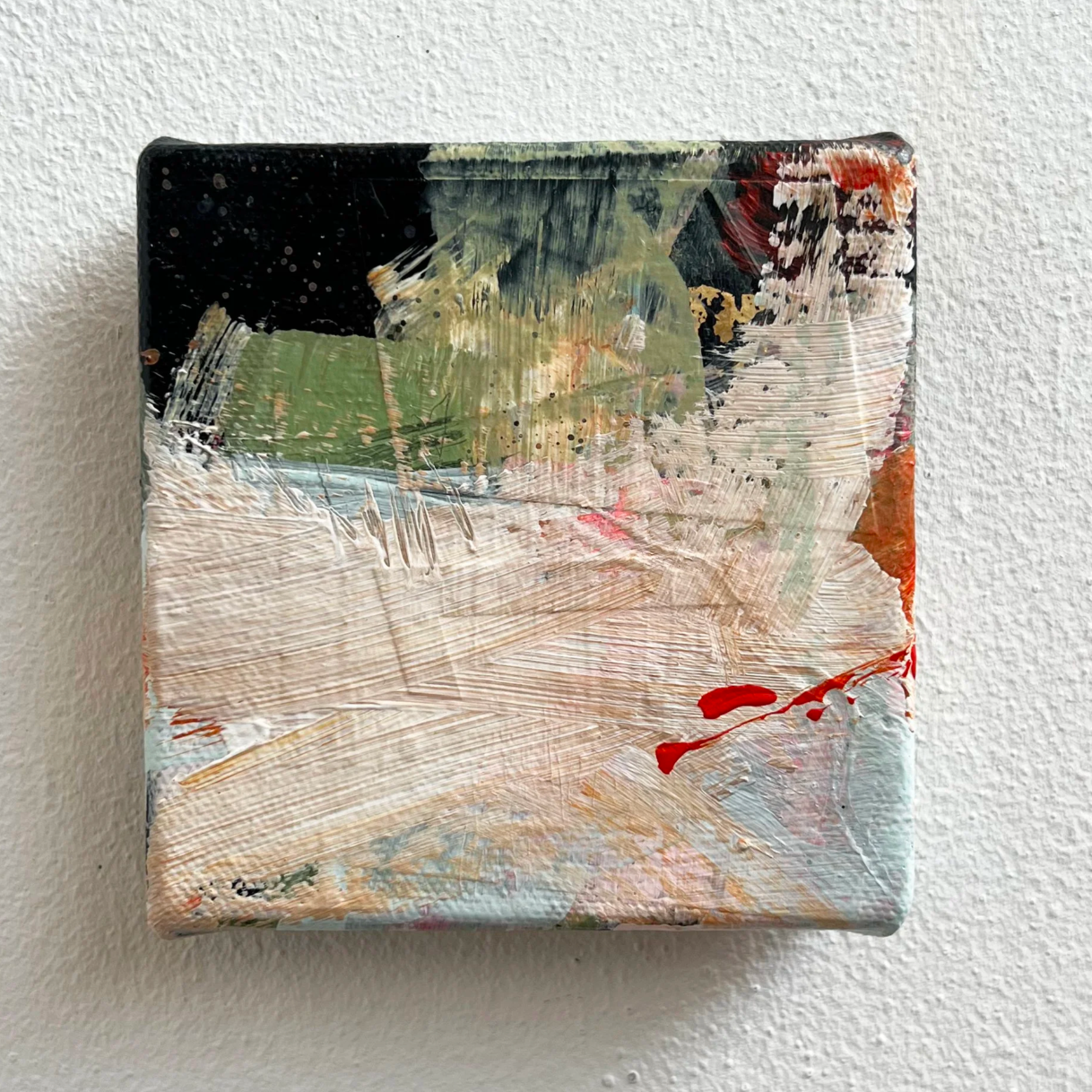 Small abstract painting with green, black, white, beige, red, and orange brushstrokes on a white textured wall.