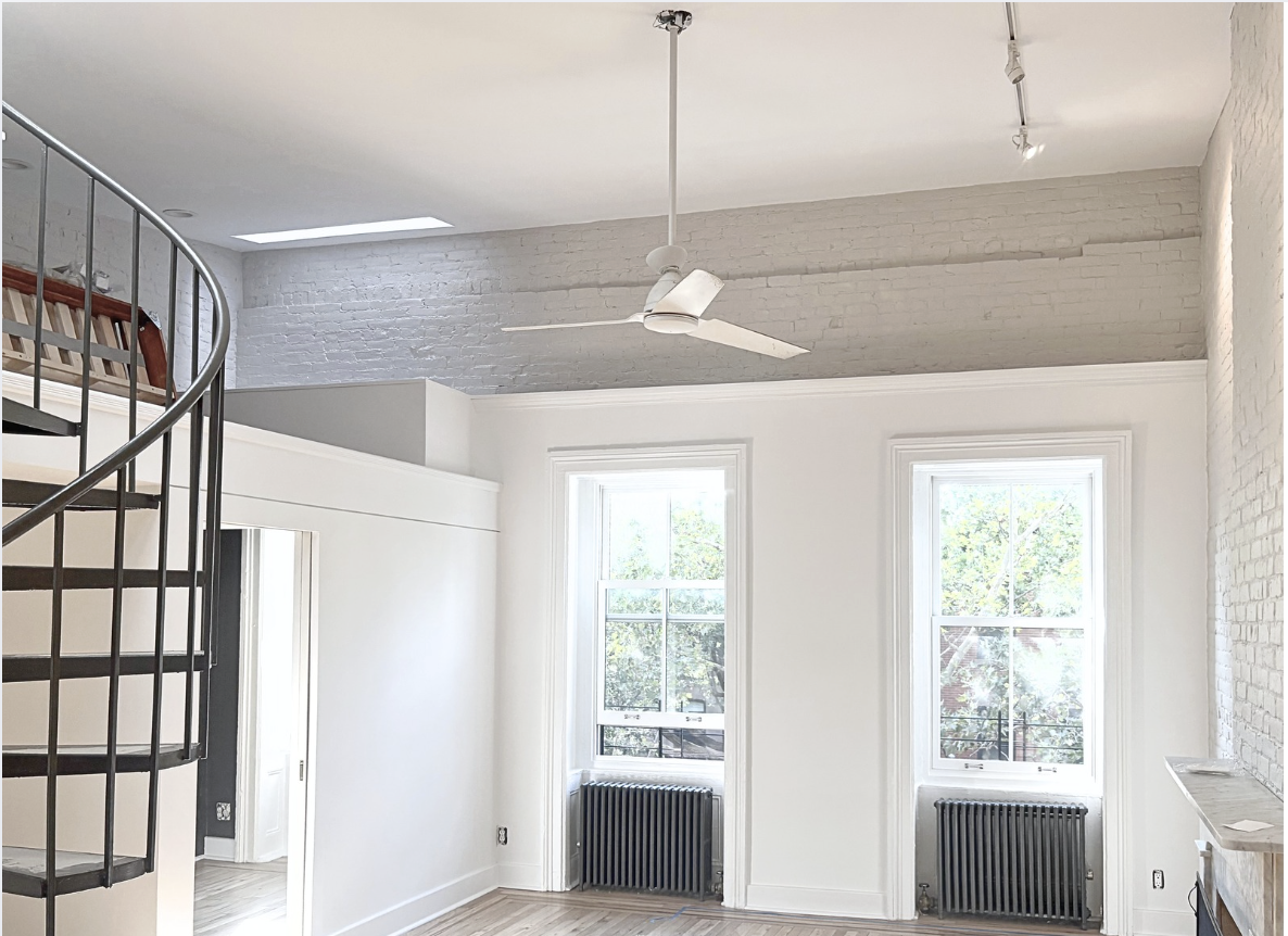 Image of a brightly lit living room and spiral staircase in a Brooklyn NYC brownstone apartment refreshed with white painted walls and brick.