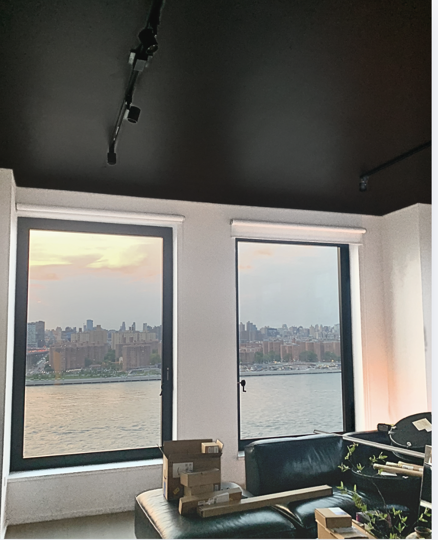 View from a high-rise NYC luxury apartment showing the East River. The ceiling has been painted dark brown to match window frames and the walls are white.