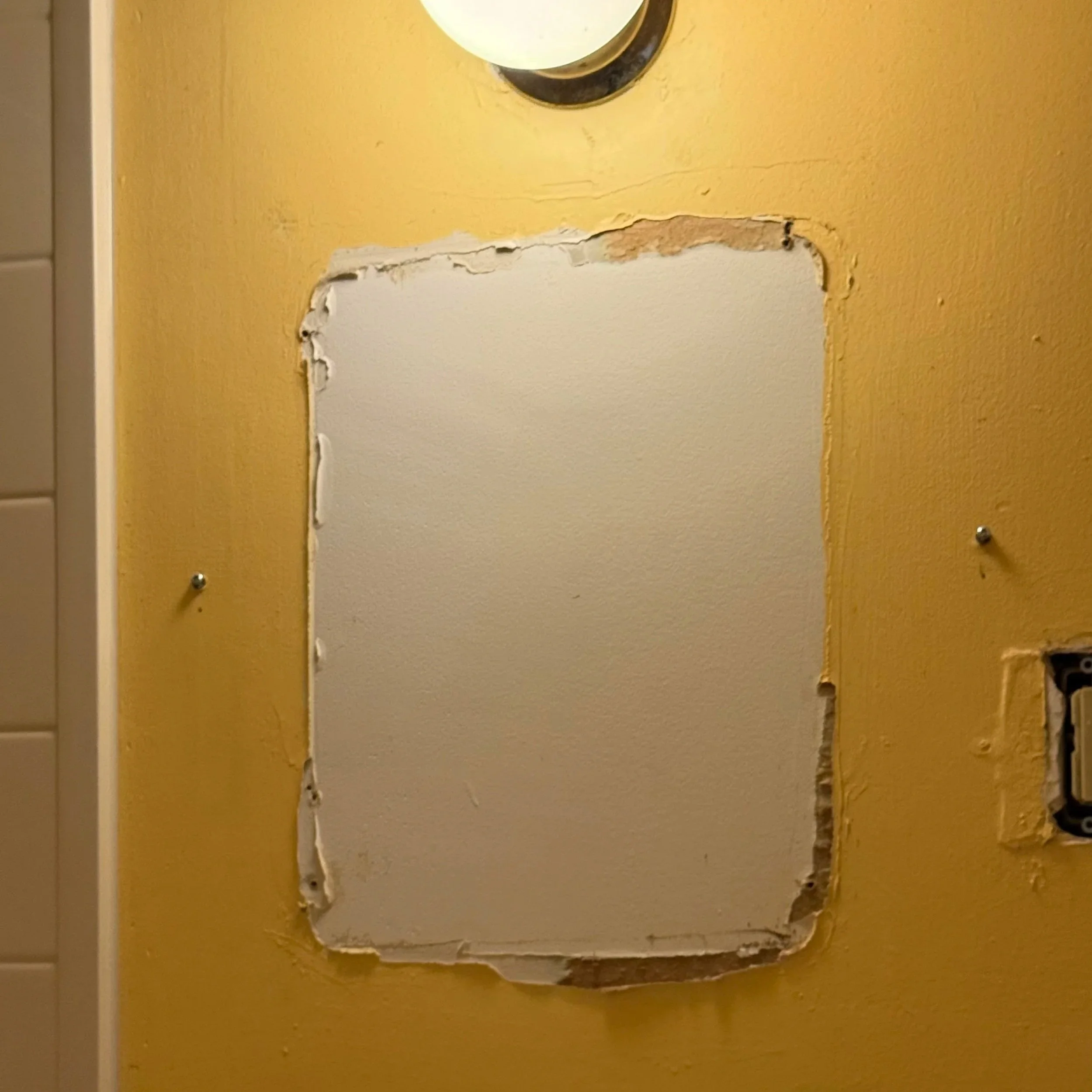 Image of a yellow painted damaged wall with holes left over after removal of a bathroom mirror requiring skim coating repair and painting