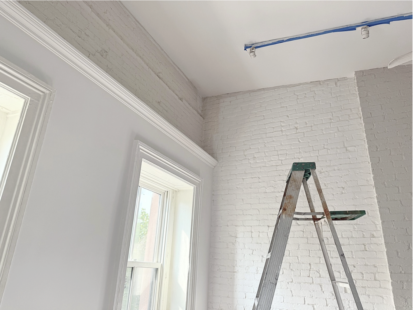 Photo of the interior of a Brooklyn Brownstone living room with white painted walls and white painted brick with a ladder in the foreground.