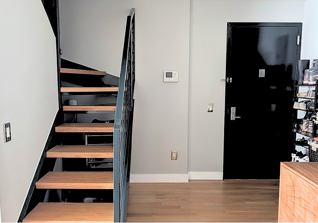 Photo of a contrasting black staircase with warm wood bases against a light gray painted wall and dark grey entryway door.